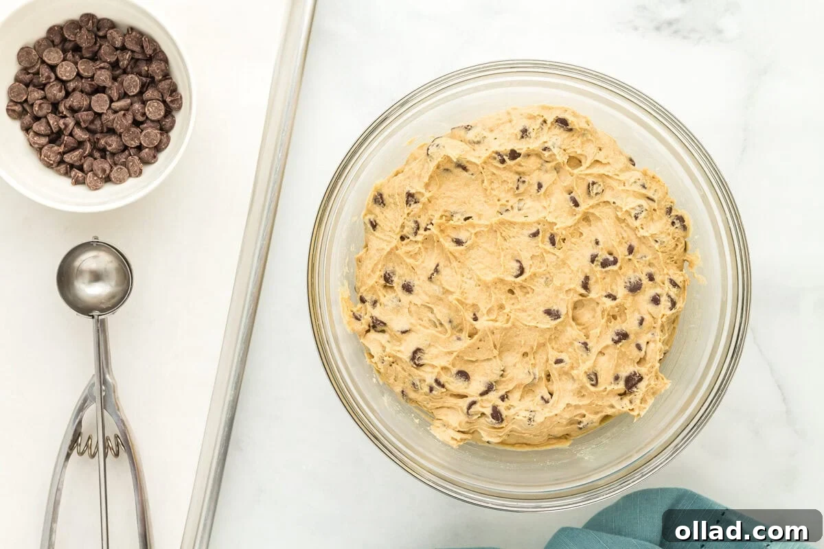 A bowl of freshly mixed oat flour chocolate chip cookie dough, covered with plastic wrap, ready for chilling.