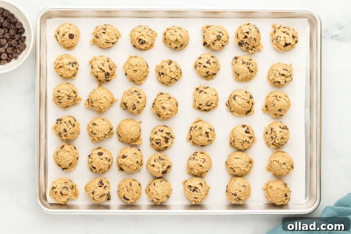 Scoops of oat flour chocolate chip cookie dough arranged on a parchment-lined baking sheet before rolling.
