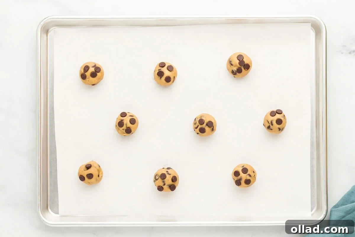 Spaced out balls of oat flour chocolate chip cookie dough on a parchment-lined baking sheet, ready for the oven.