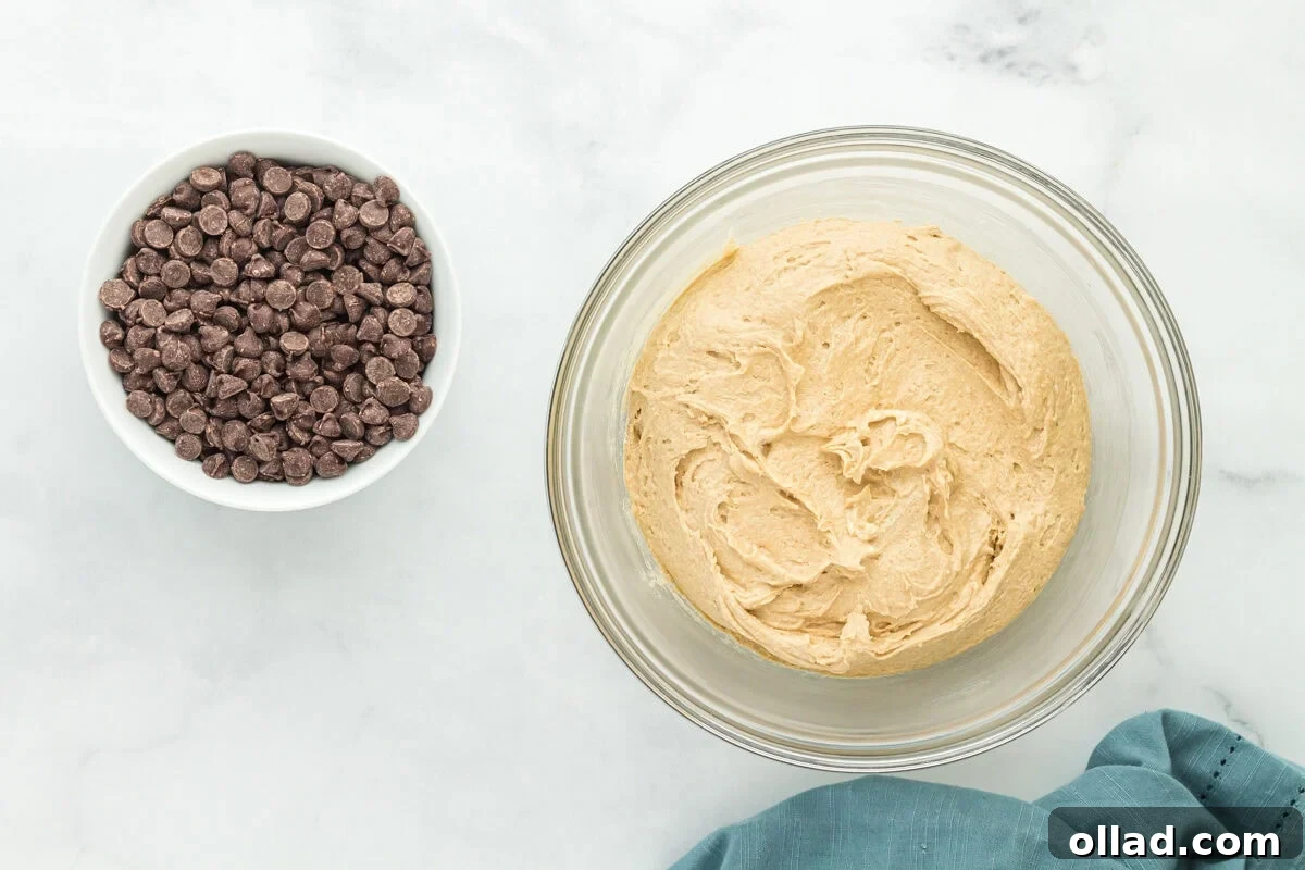 Oat flour chocolate chip cookie dough in a bowl with a bowl of semi-sweet chocolate chips ready to be folded in.