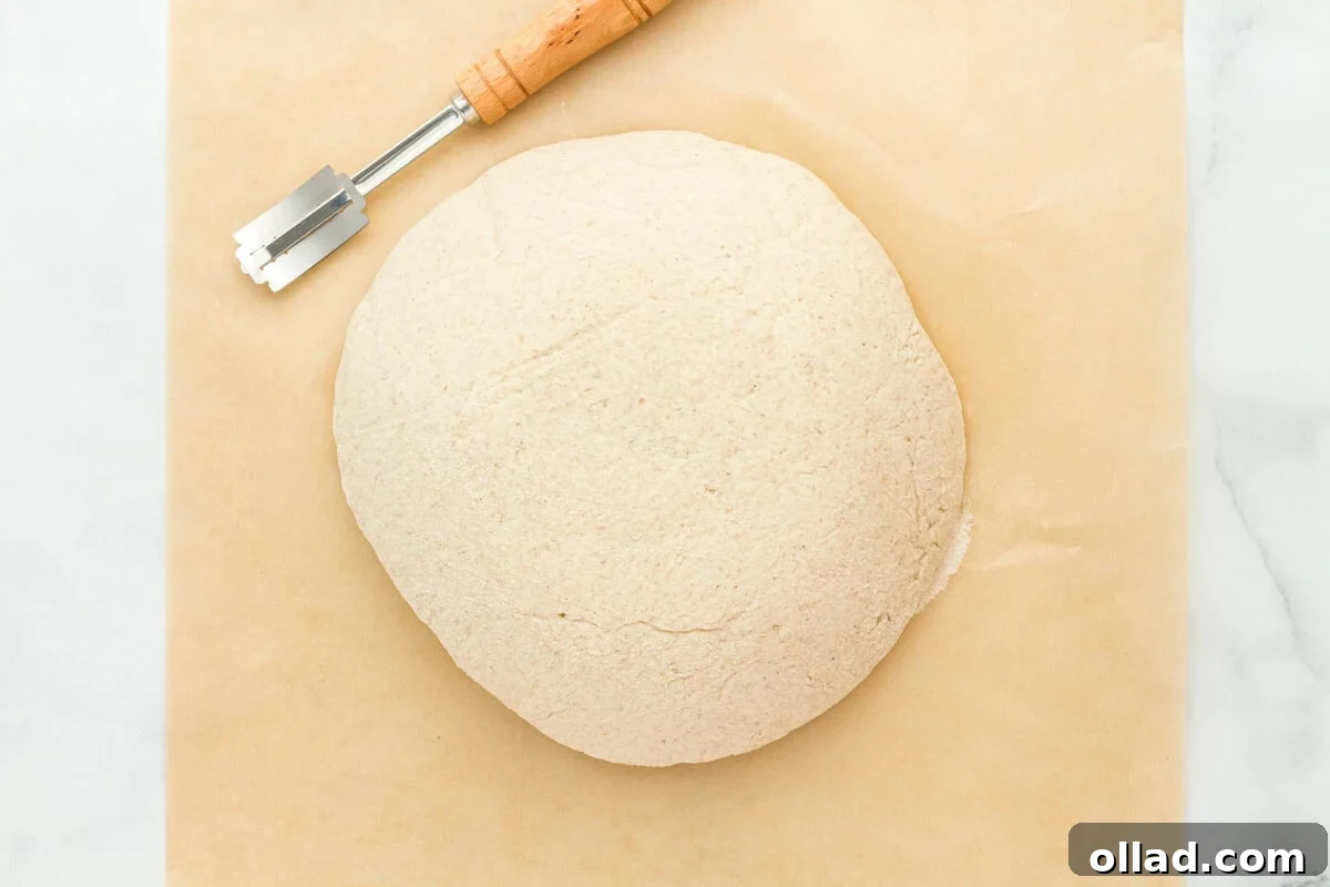 The risen gluten-free sourdough bread dough placed on a cutting board, ready for scoring with a lame, showing its smooth, proofed surface.