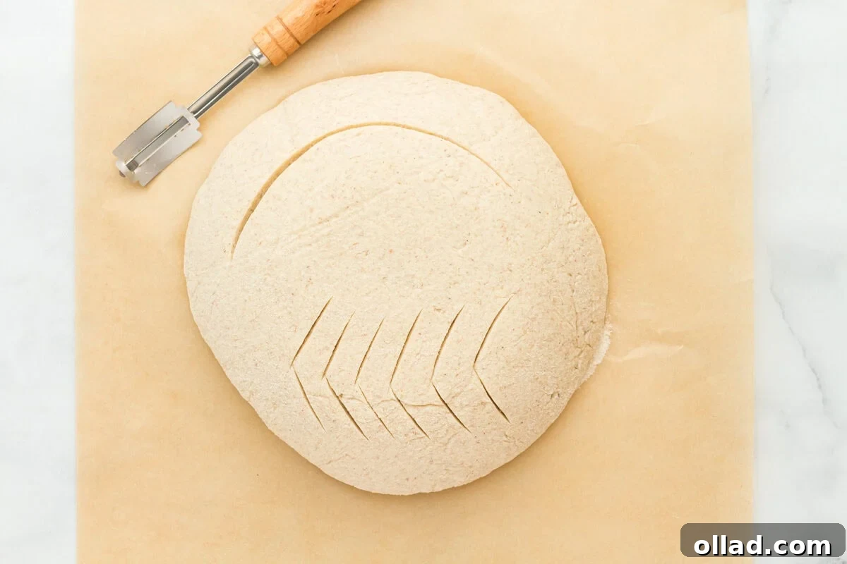 Gluten-free sourdough bread dough, intricately scored with a lame, revealing deep cuts across its surface before baking.