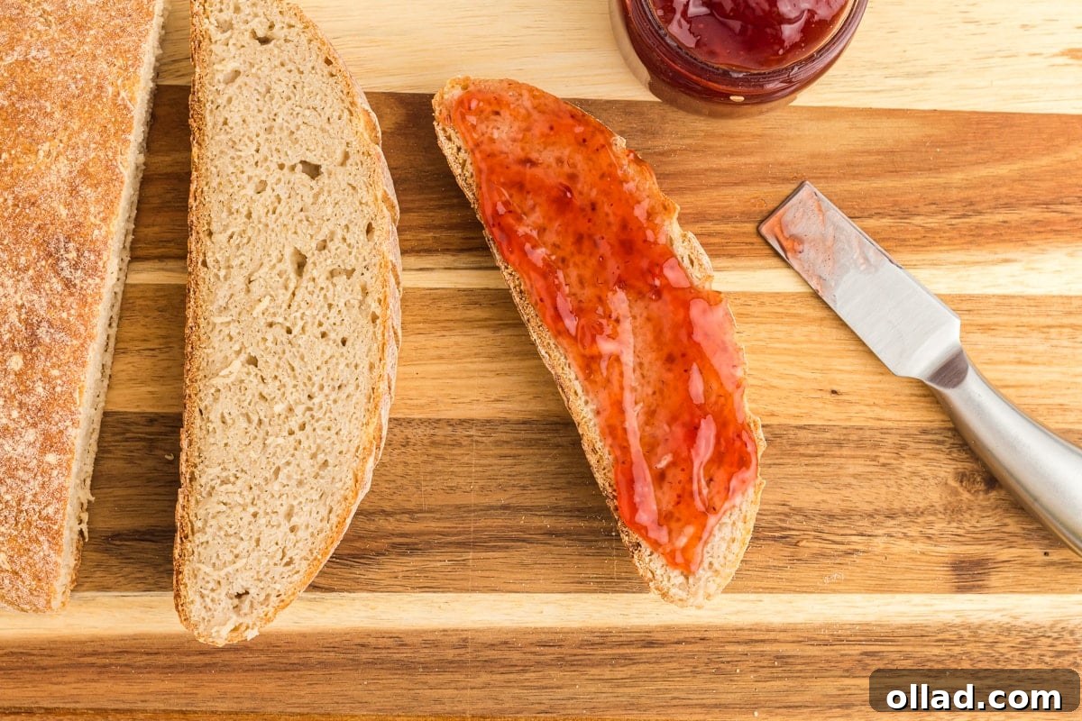 Multiple slices of golden-brown gluten-free sourdough bread neatly arranged on a wooden cutting board, alongside a knife and a jar of jam, highlighting its inviting texture.