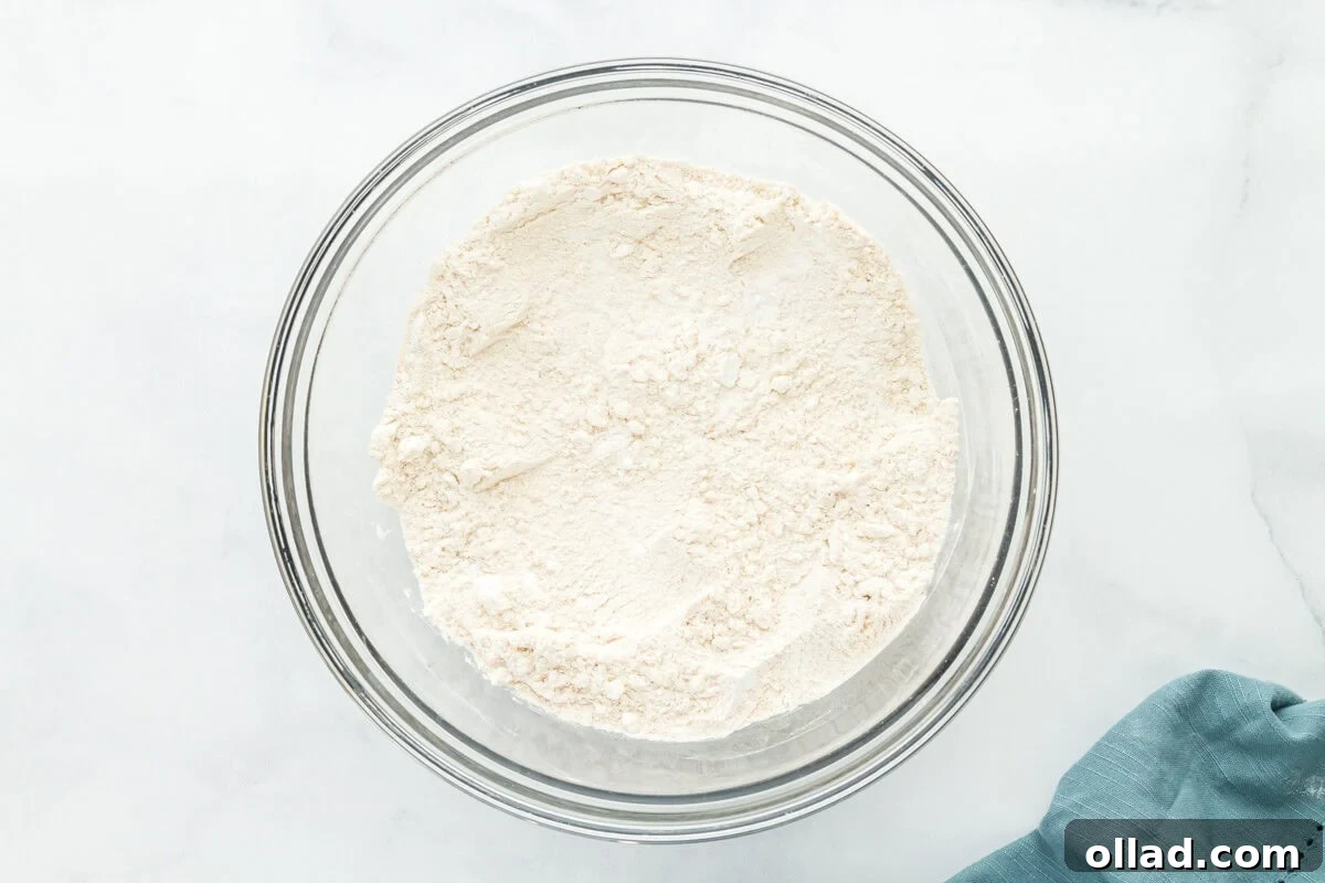 Various dry ingredients for gluten-free sourdough bread, including potato starch, sorghum flour, brown rice flour, tapioca flour, and salt, combined in a clear glass bowl.