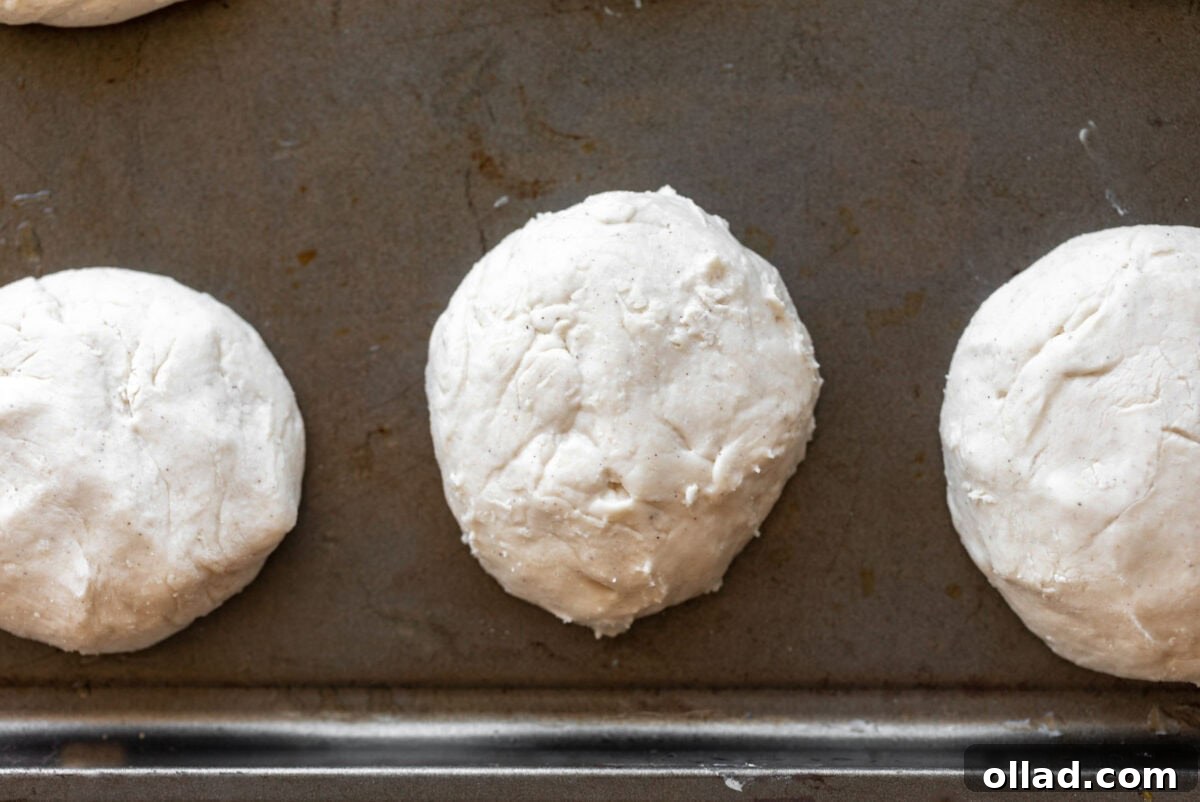 Gluten-free English muffin dough balls neatly arranged on a baking sheet.