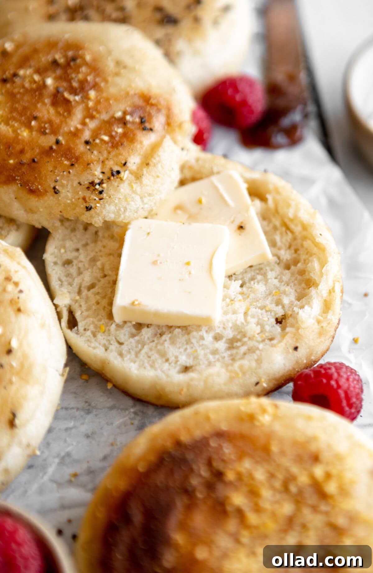 A gluten-free English muffin split open with pats of butter melting into its craggy surface.