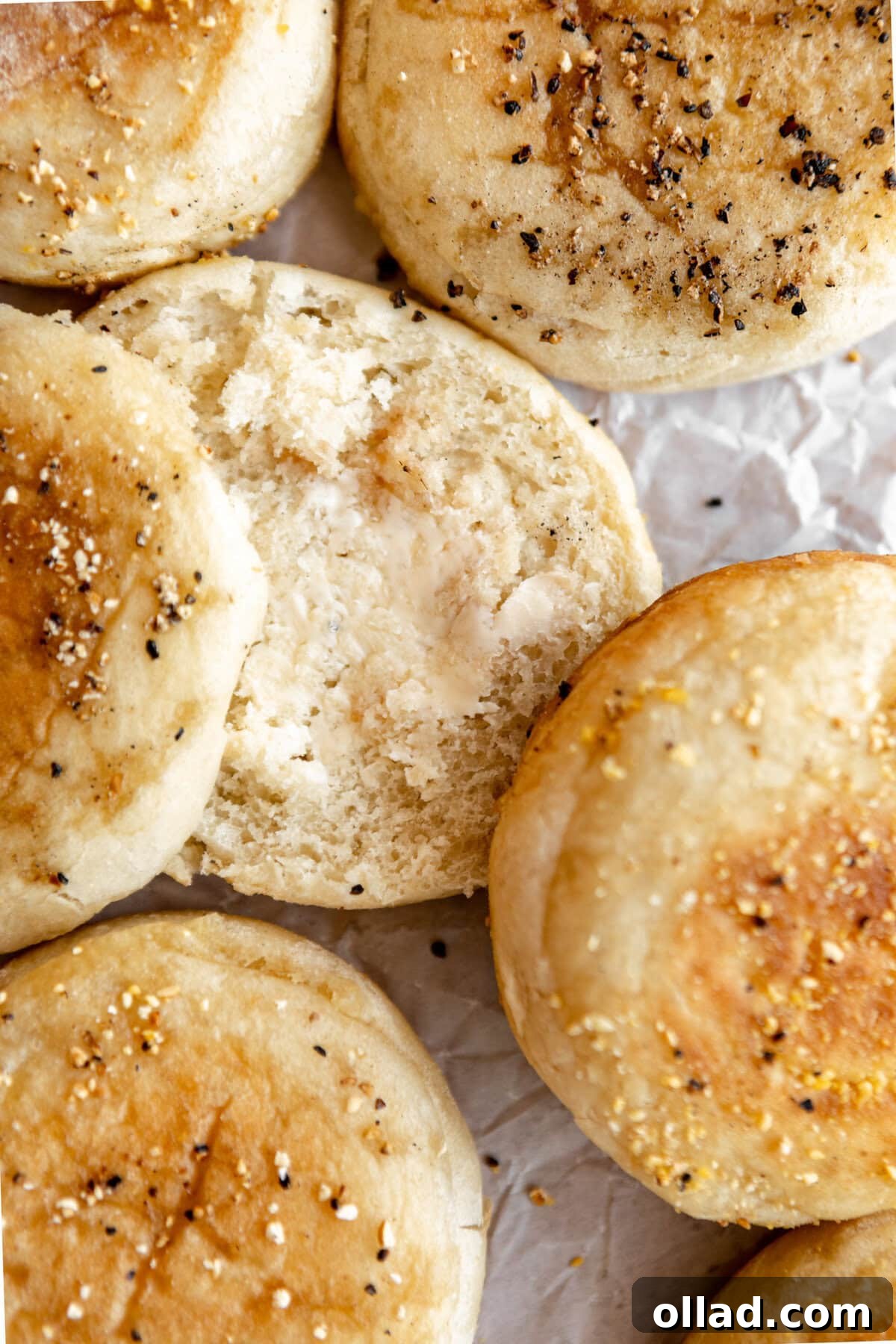 A gluten-free English muffin, perfectly split open, with melted butter spread generously across its surface.