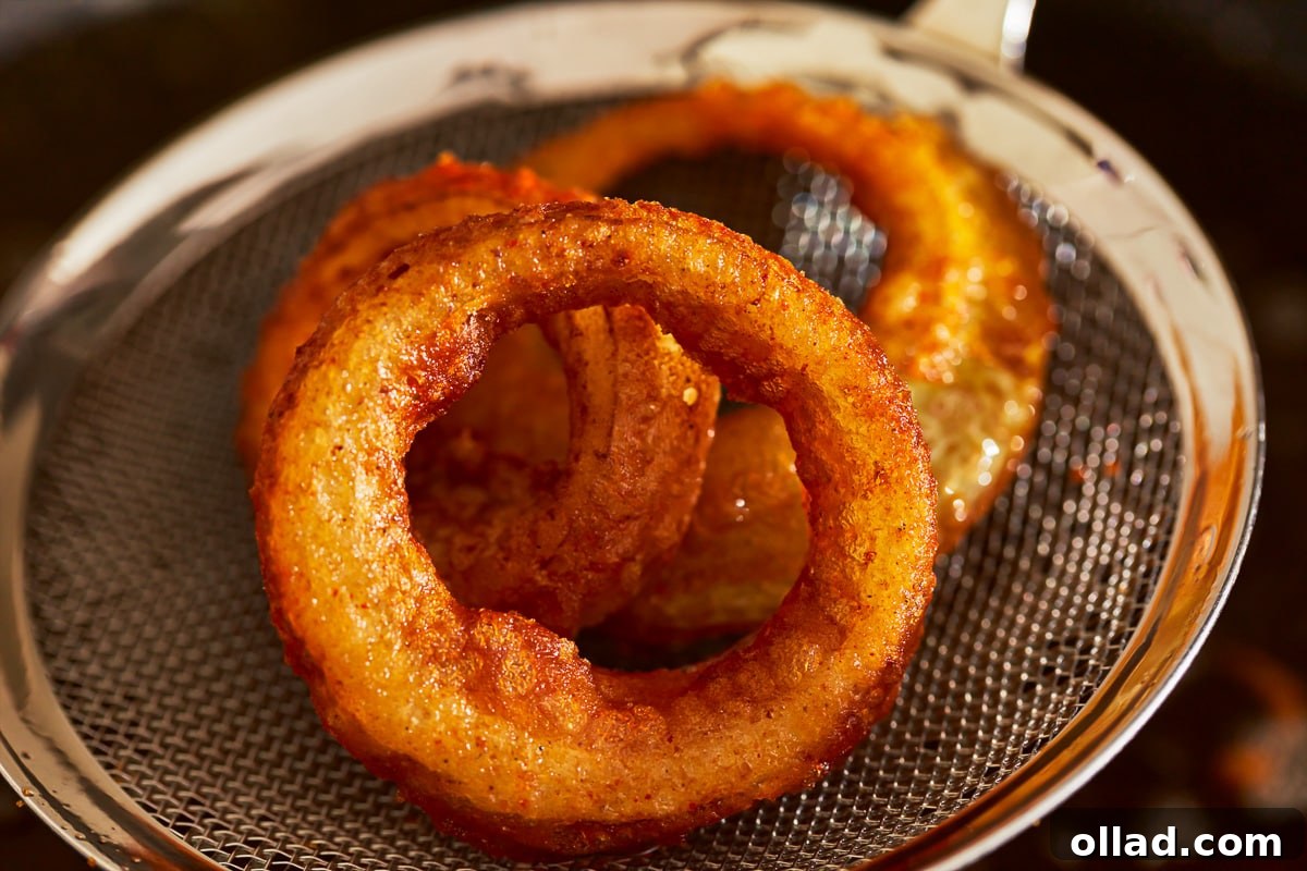 Crispy Gluten-Free Onion Rings 11 A close-up shot of golden-brown, crispy gluten-free onion rings being removed from the hot oil with a slotted spoon, ready to drain.