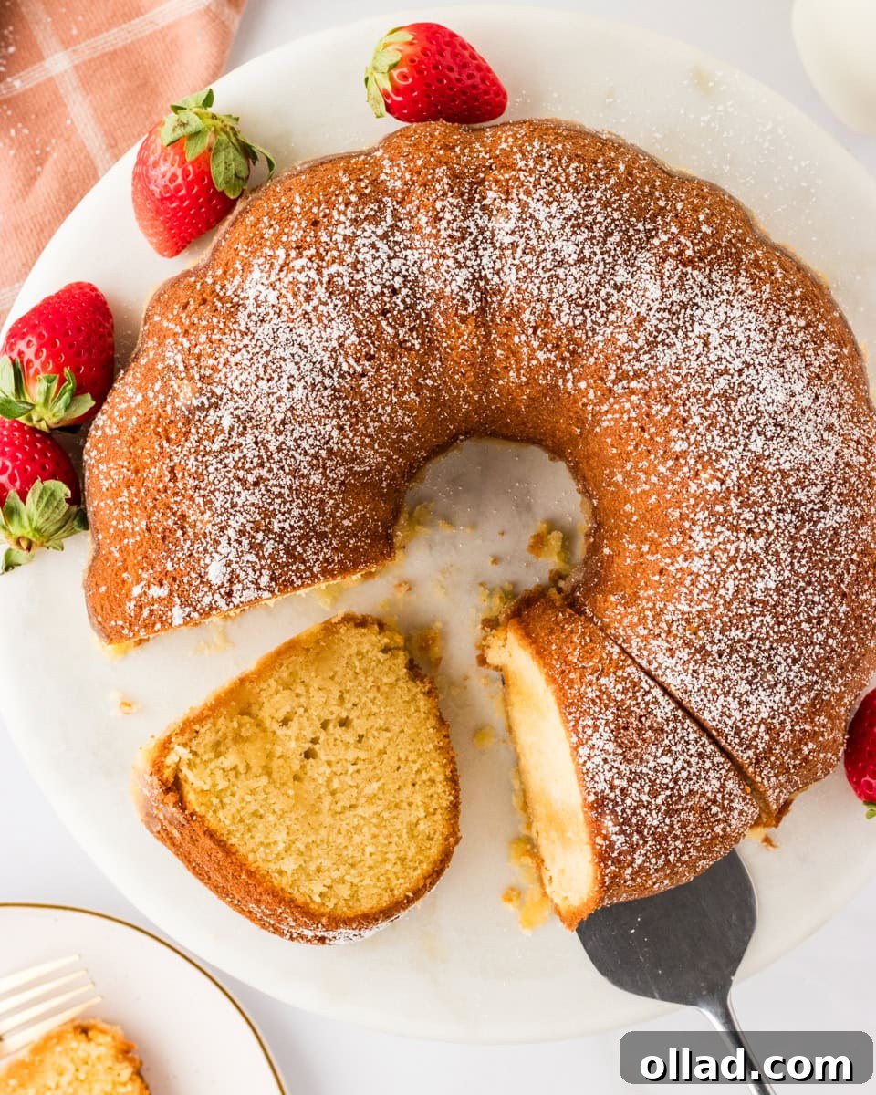 Irresistible Gluten-Free Cake Secrets 18 A Gluten-Free Kentucky Butter Pound Cake on a round white platter, topped with powdered sugar and garnished with fresh strawberries. A slice has been cut and partially removed, showcasing the cake's golden interior.