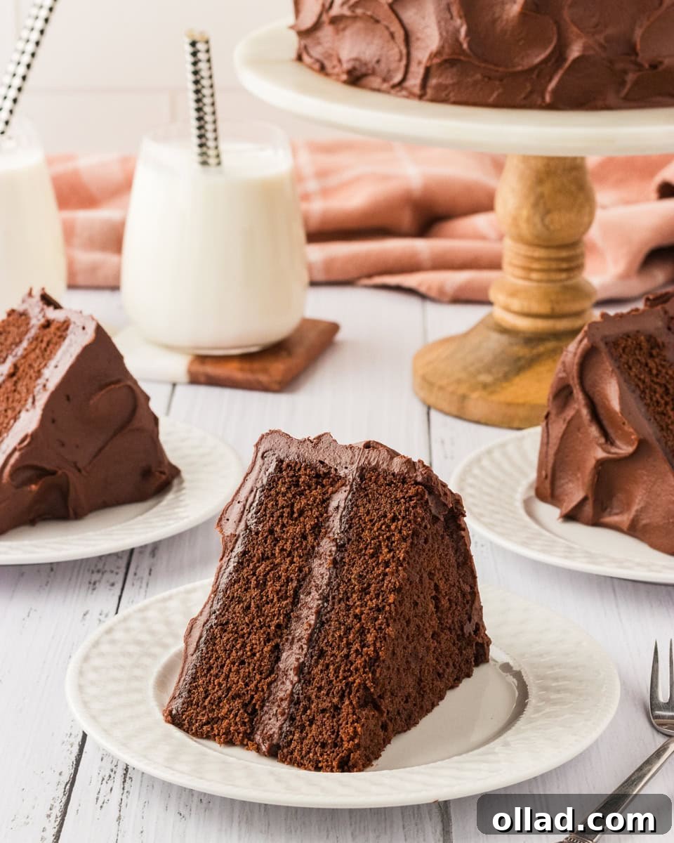 Irresistible Gluten-Free Cake Secrets 3 A slice of rich, two-layer chocolate cake with creamy chocolate frosting, served on a white plate. A full cake sits on a wooden cake stand in the background, with additional slices plated and glasses of milk nearby.