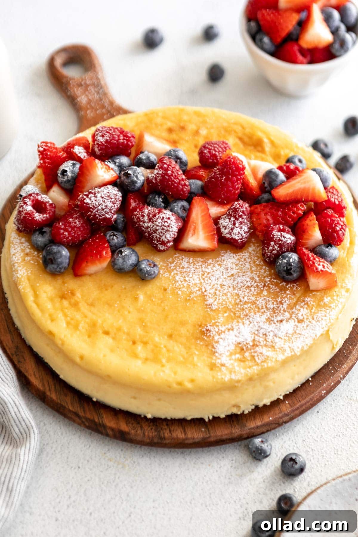 crustless cheesecake on a cake board topped with fruit and powdered sugar.