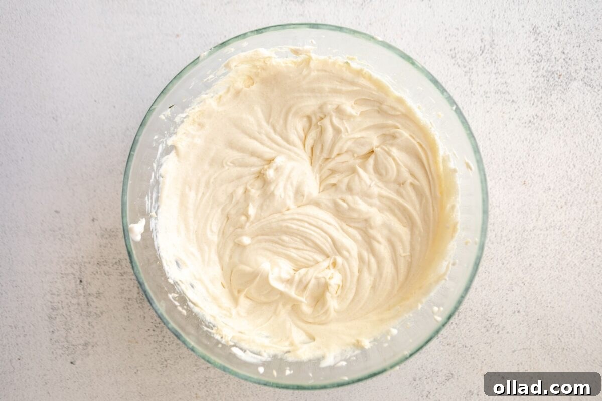 Smooth cheesecake batter after mixing in sugar, sour cream, and vanilla, in a glass mixing bowl.