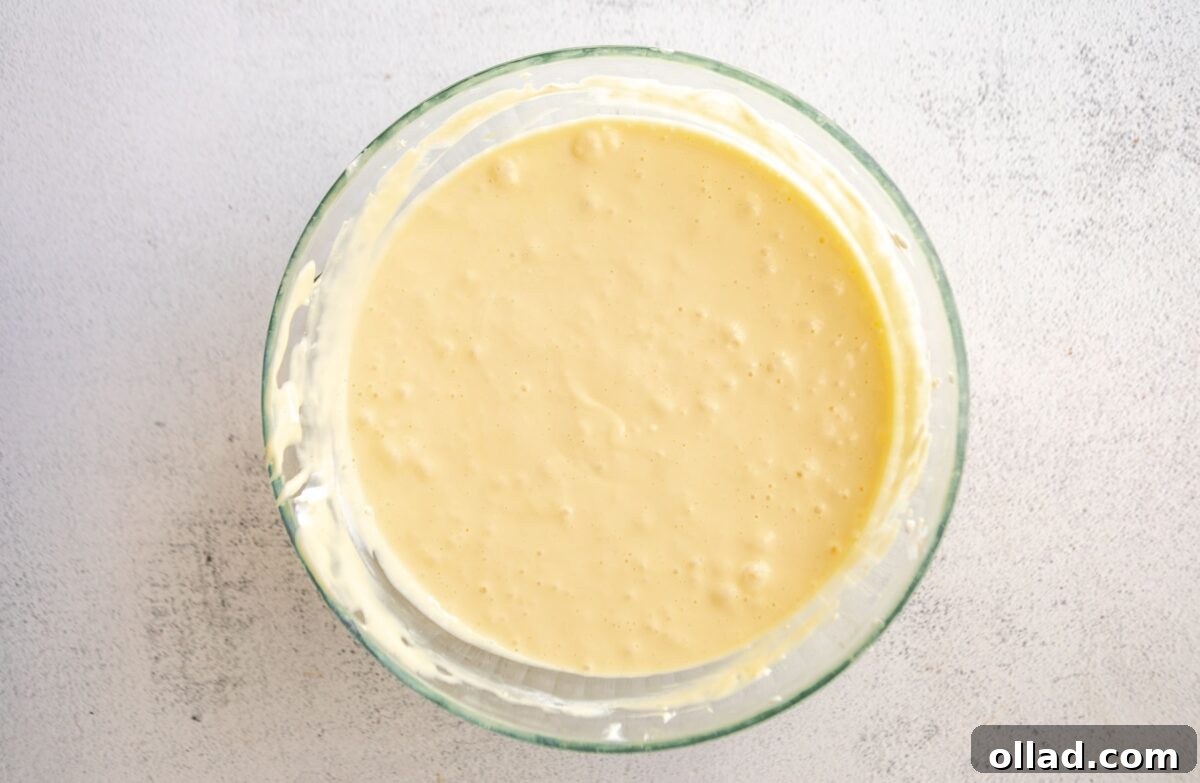 Fully mixed cheesecake batter with eggs incorporated, smooth and pourable in a glass bowl.