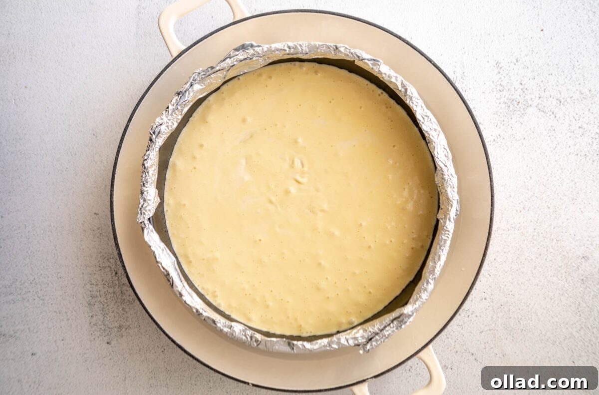 heesecake batter poured into a parchment- and foil-lined springform pan, ready to be baked in a water bath.