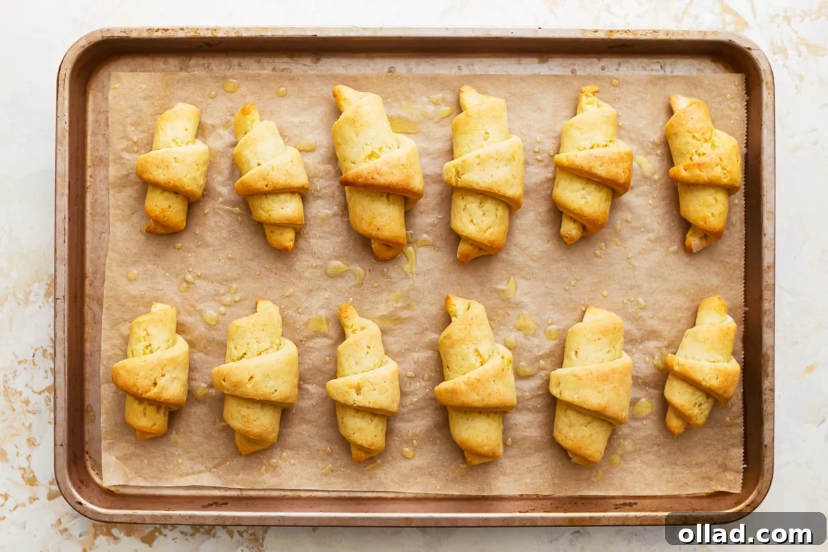 Freshly baked gluten-free crescent rolls on a baking sheet, brushed with melted butter.