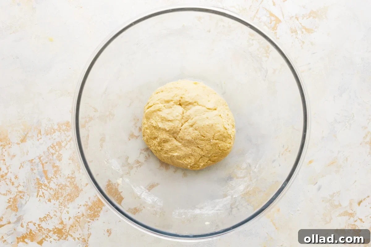 Gluten-free crescent roll dough resting in a glass bowl, covered with plastic wrap.