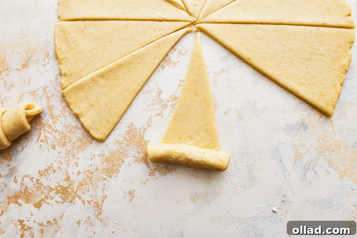 A gluten-free crescent roll triangle being carefully rolled up from base to tip.