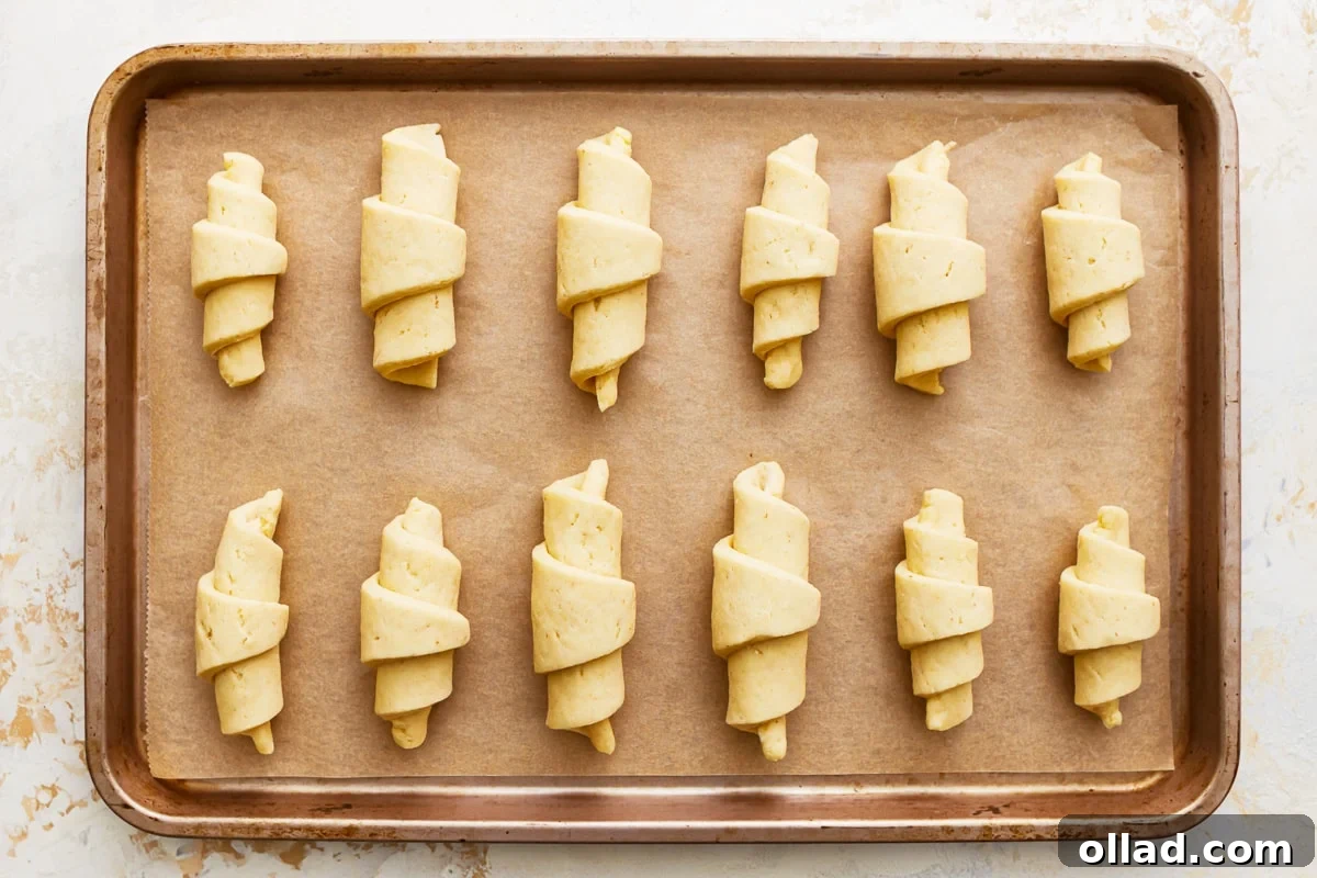 Unbaked gluten-free crescent rolls arranged on a parchment-lined baking sheet, proofing.