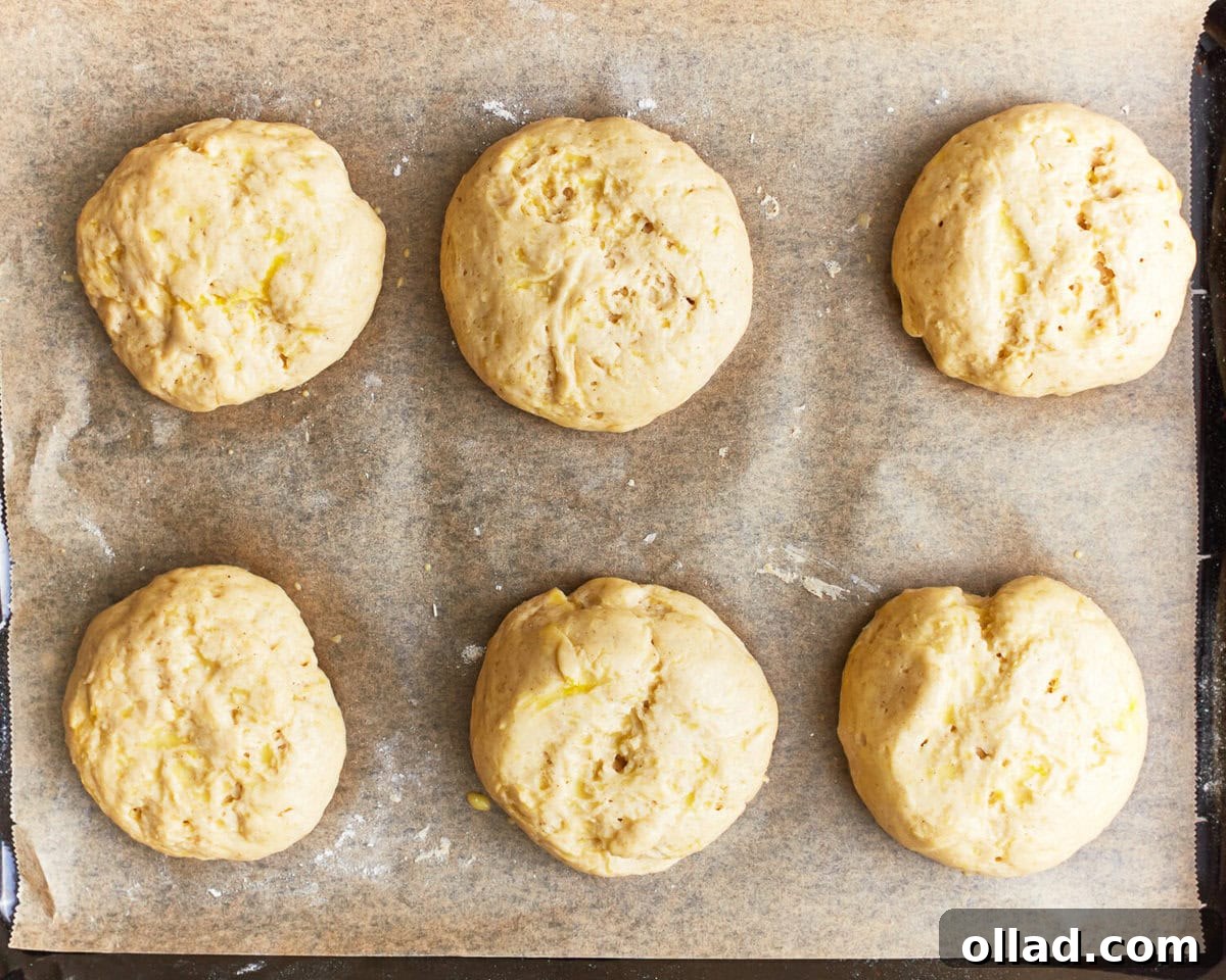 risen shaped gluten-free hamburger bun dough on a baking sheet.