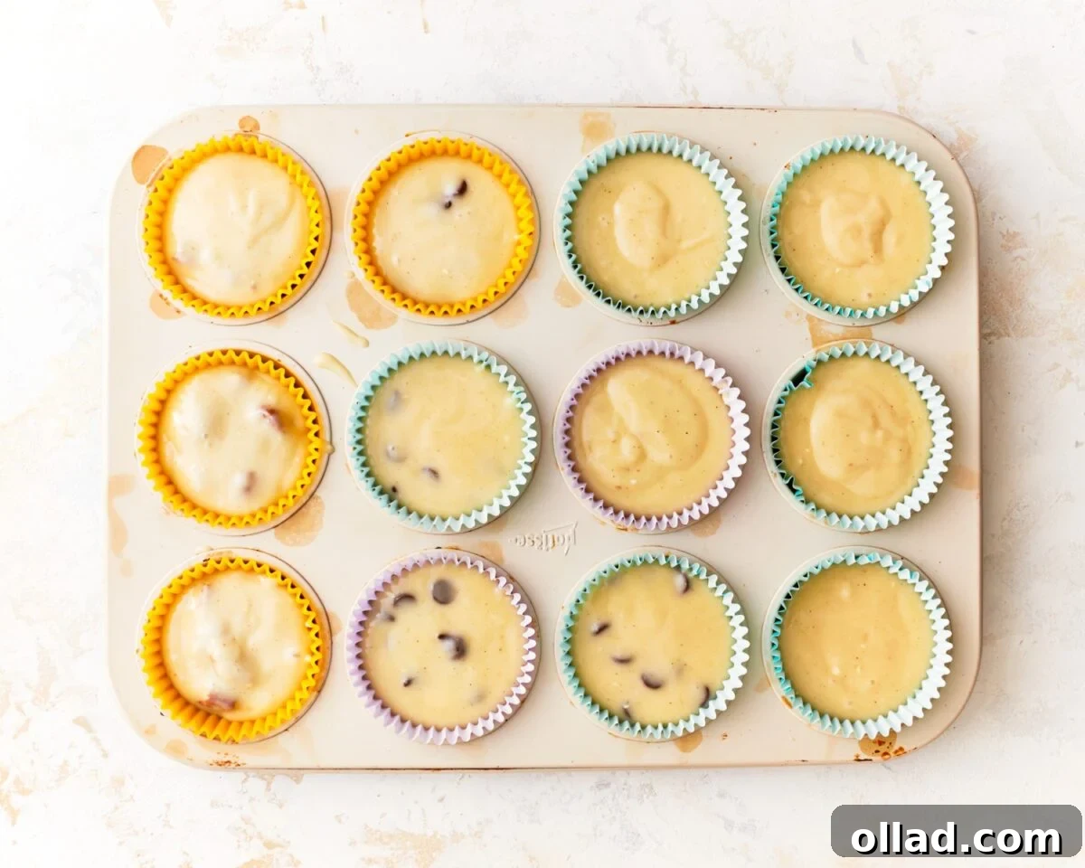 Irresistible Gluten-Free Muffins 6 A standard muffin pan precisely lined with colorful paper wrappers, each cup filled approximately three-quarters full with the prepared gluten-free muffin batter, some visibly containing chocolate chips.