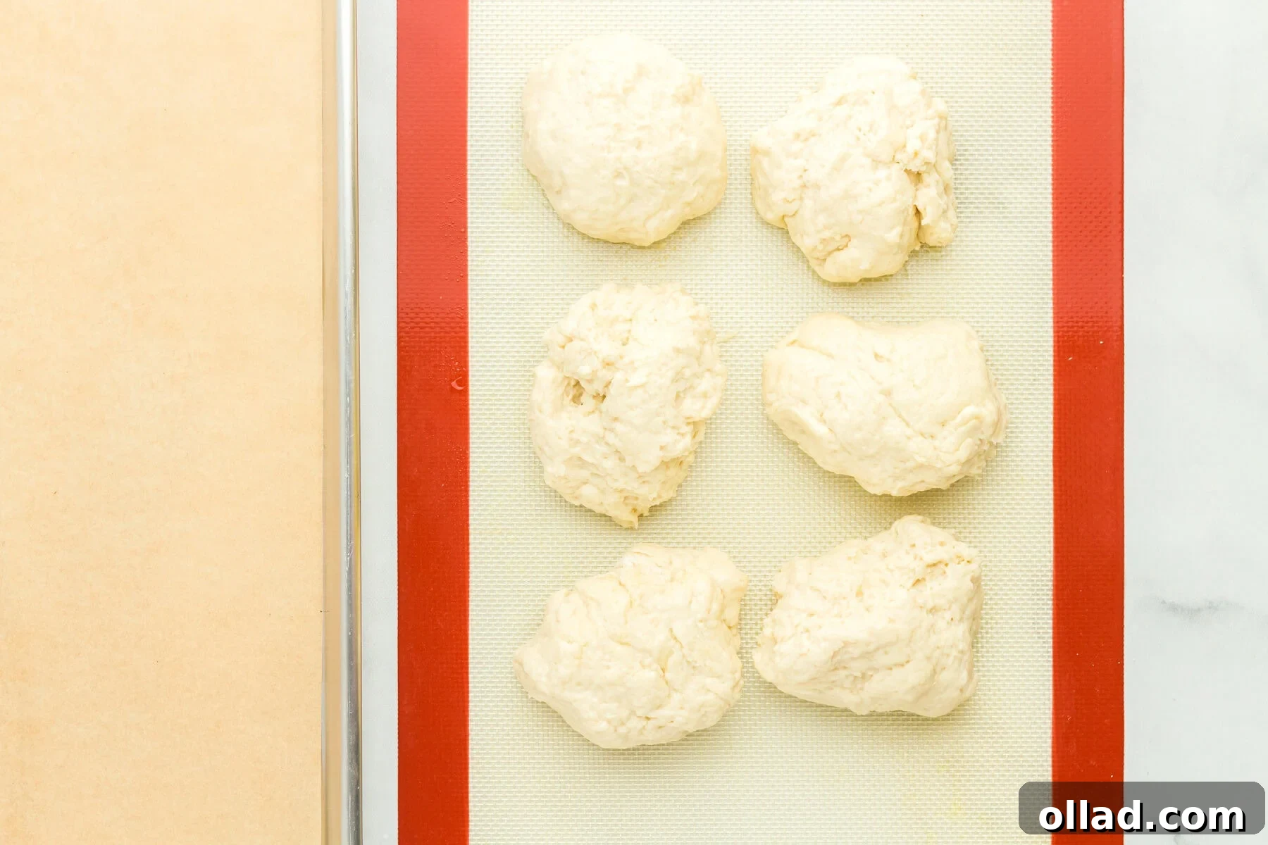 A large mass of gluten-free hot dog bun dough divided into six equal portions on an oiled surface.