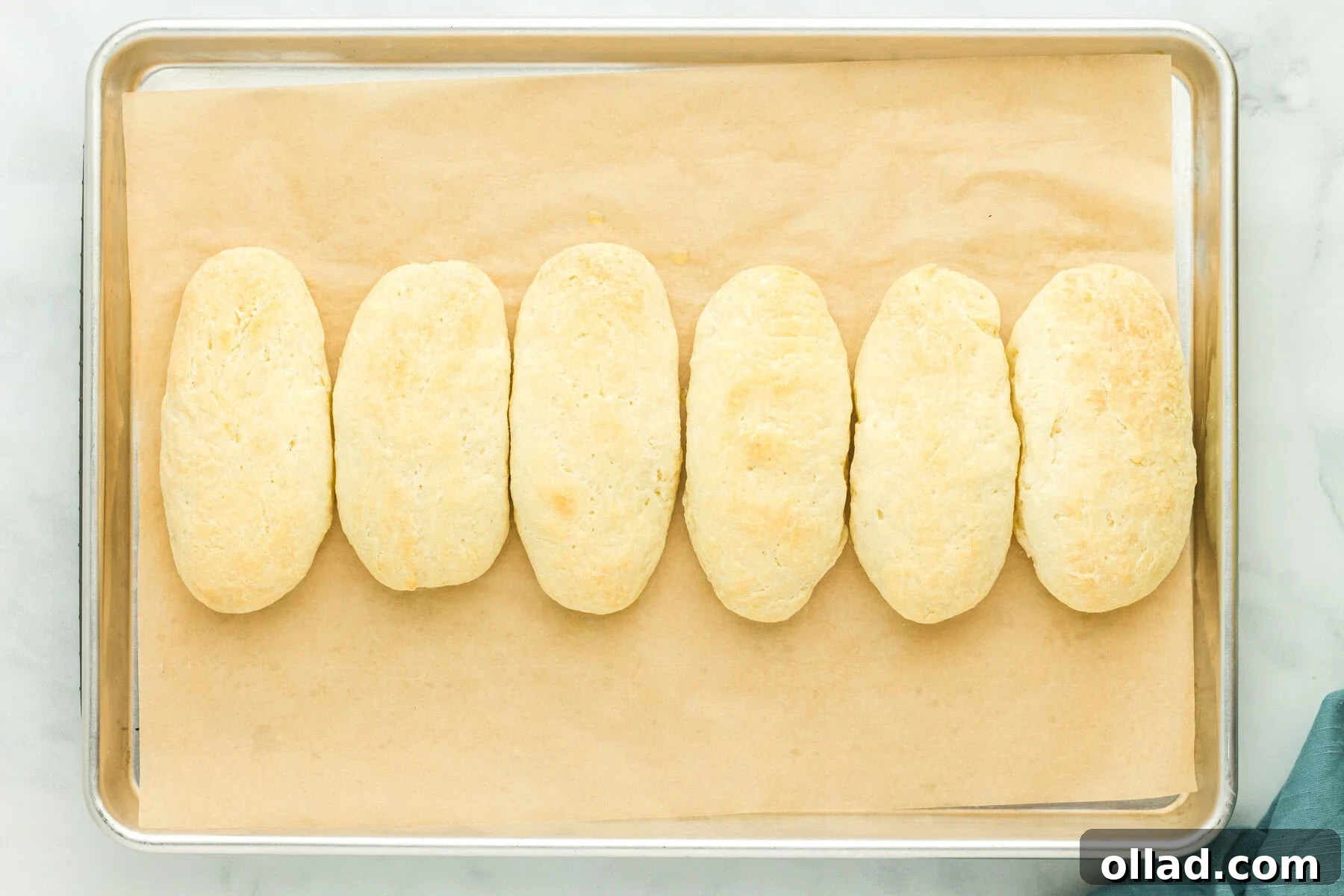 Freshly baked golden-brown gluten-free hot dog buns on a parchment-lined baking sheet, just out of the oven.