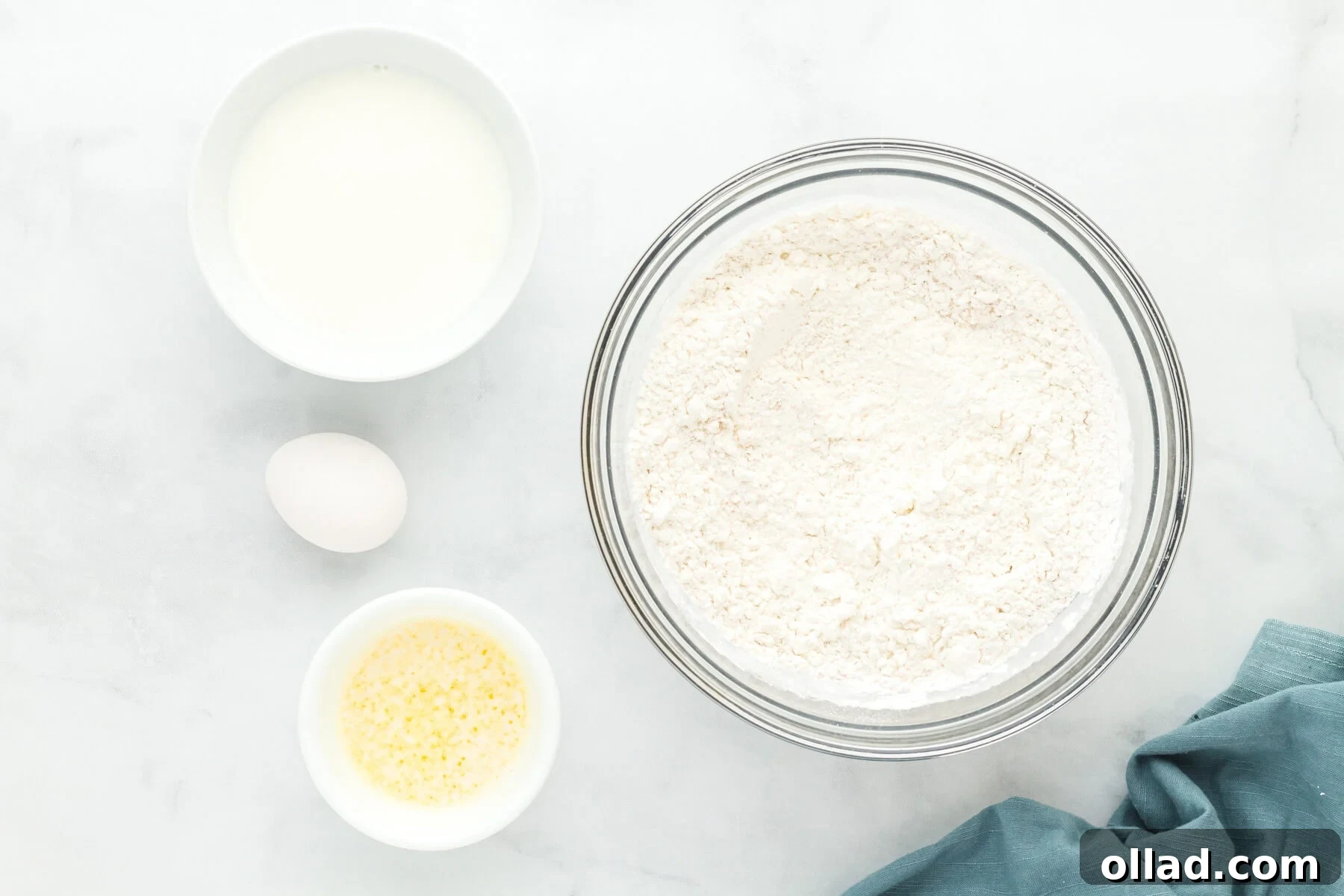 Dry ingredients for gluten-free hot dog buns, including flour, sugar, and yeast, in a clear glass mixing bowl.
