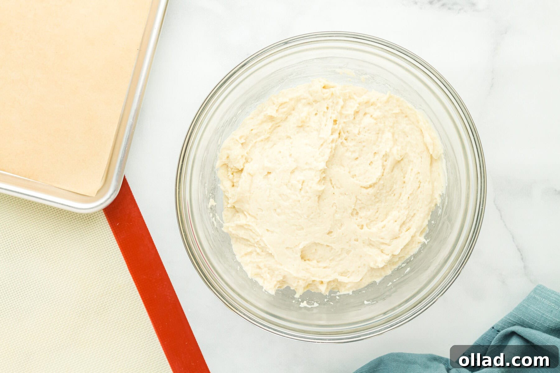 Gluten-free hot dog bun dough, wet ingredients mixed with dry, in a glass mixing bowl.