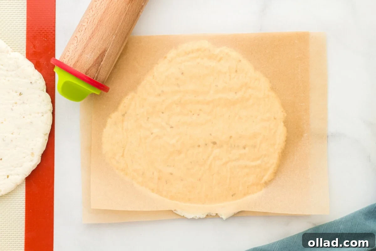 Pillowy Gluten-Free Flatbread 7 gluten-free flatbread dough rolled out between pieces of parchment paper with a rolling pin in the upper corner