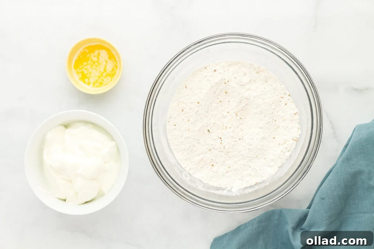Pillowy Gluten-Free Flatbread 4 Ingredients for making gluten-free flatbread, including a bowl of flour mixture, a small bowl of melted butter, and a small bowl of yogurt, arranged on a white marble surface with a blue cloth napkin