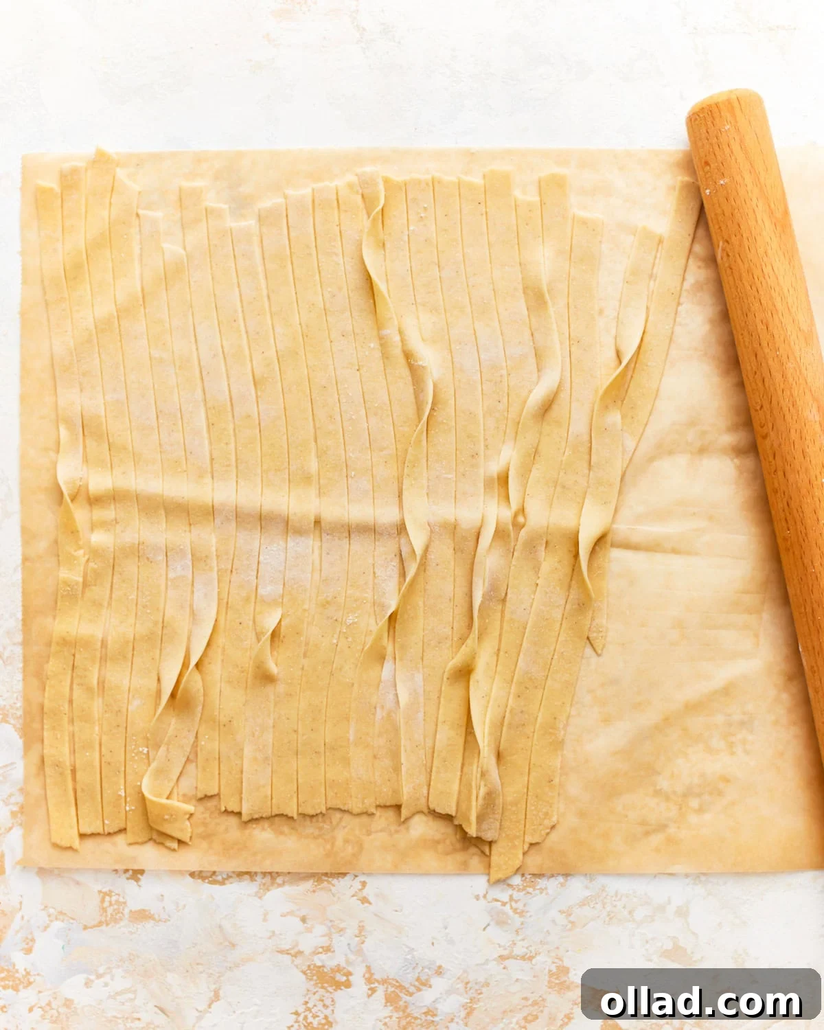 Rolled gluten-free pasta dough being cut into strips with a pizza cutter.