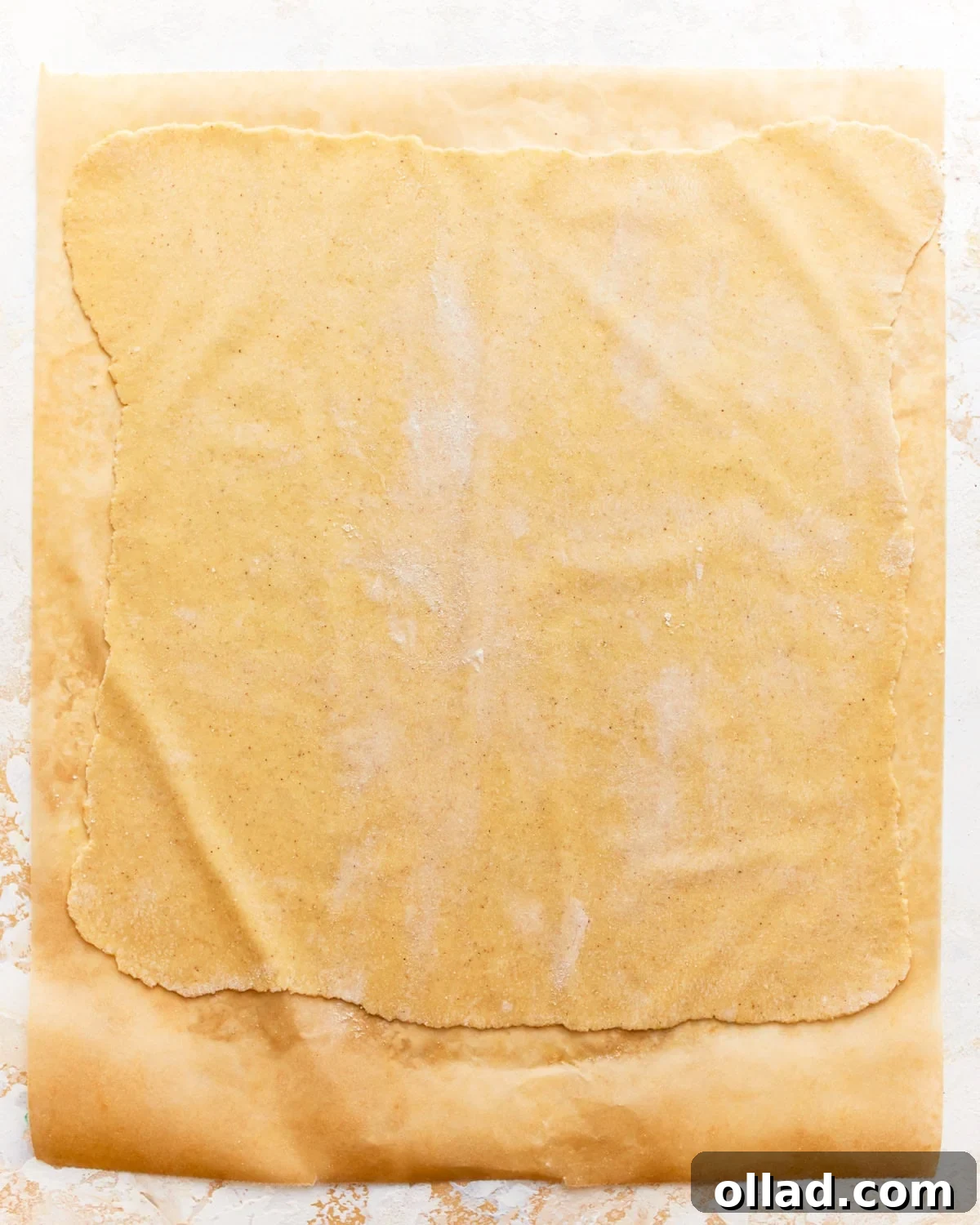 A thin, rolled-out sheet of gluten-free pasta dough on parchment paper.