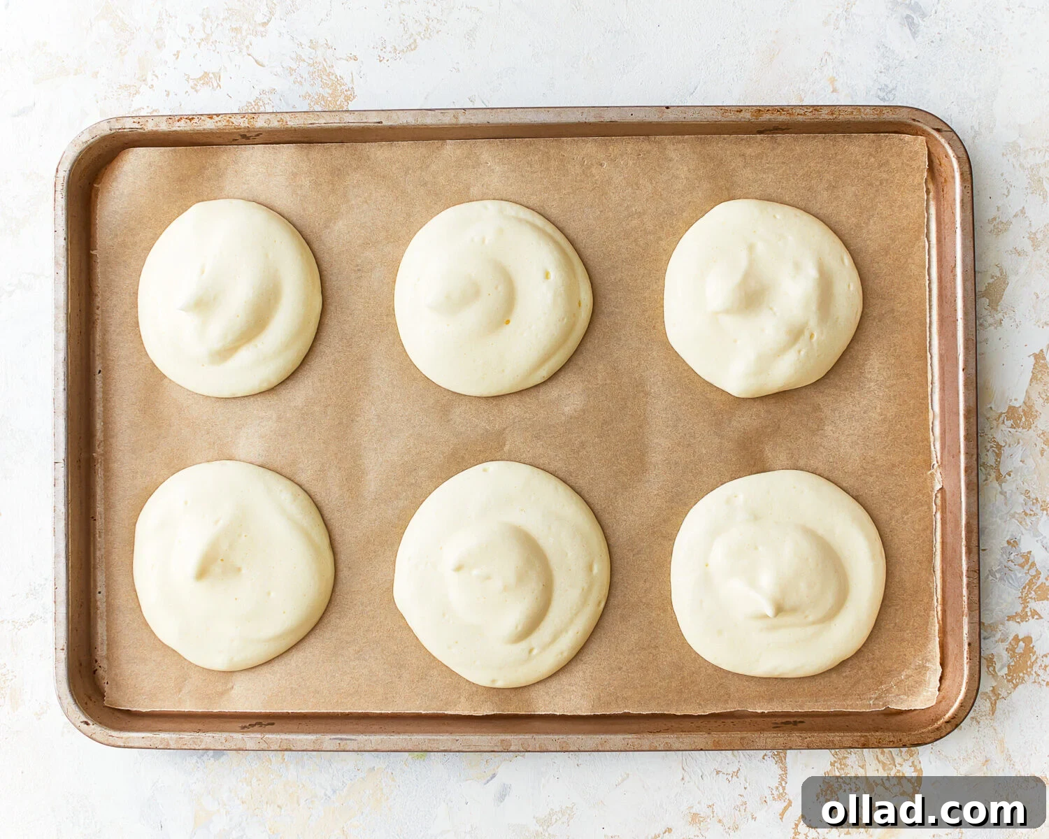 Six rounds of cloud bread batter carefully spooned onto a parchment-lined baking sheet, spaced for even baking.