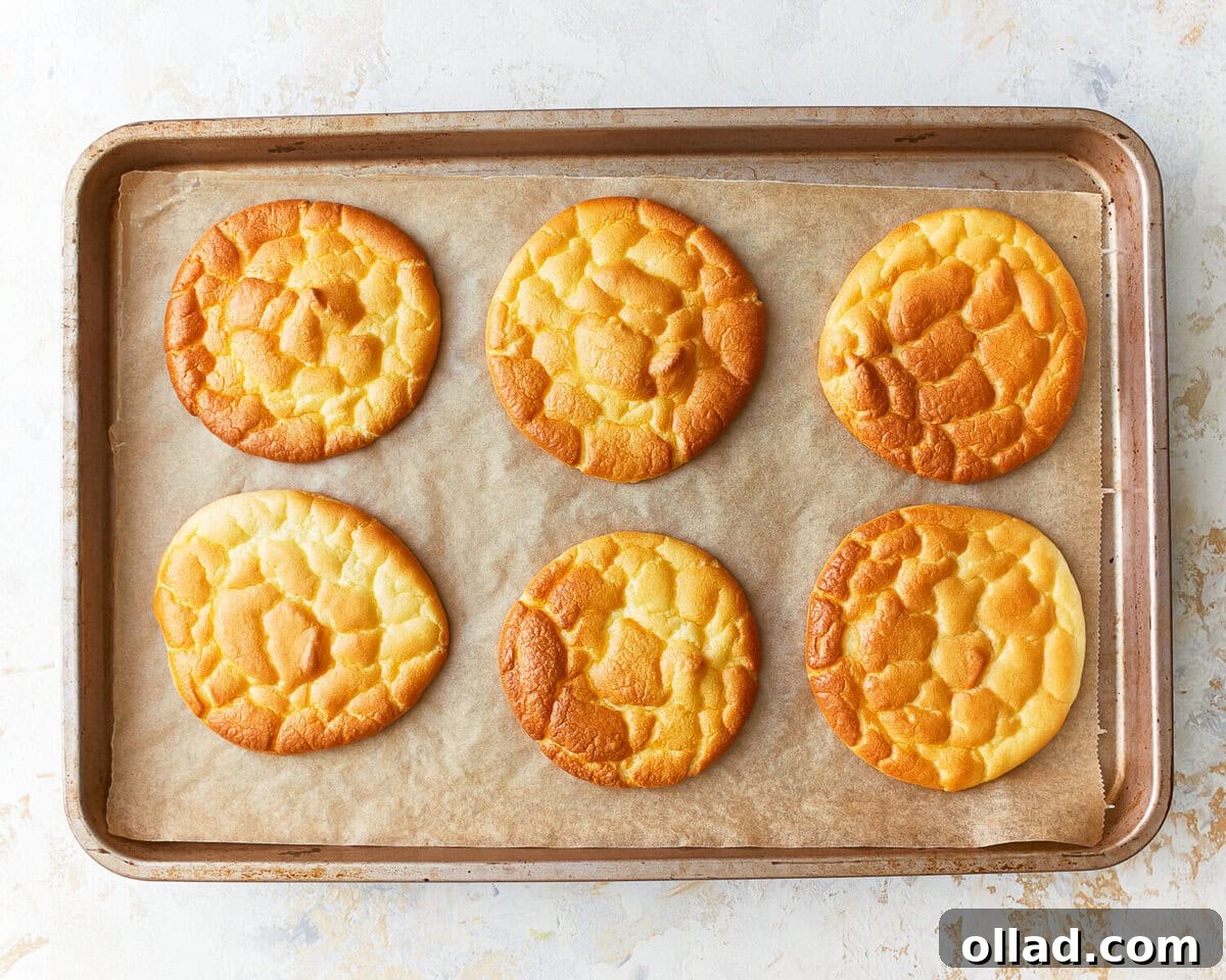 Six freshly baked slices of golden-brown cloud bread cooling on a parchment-lined baking sheet.