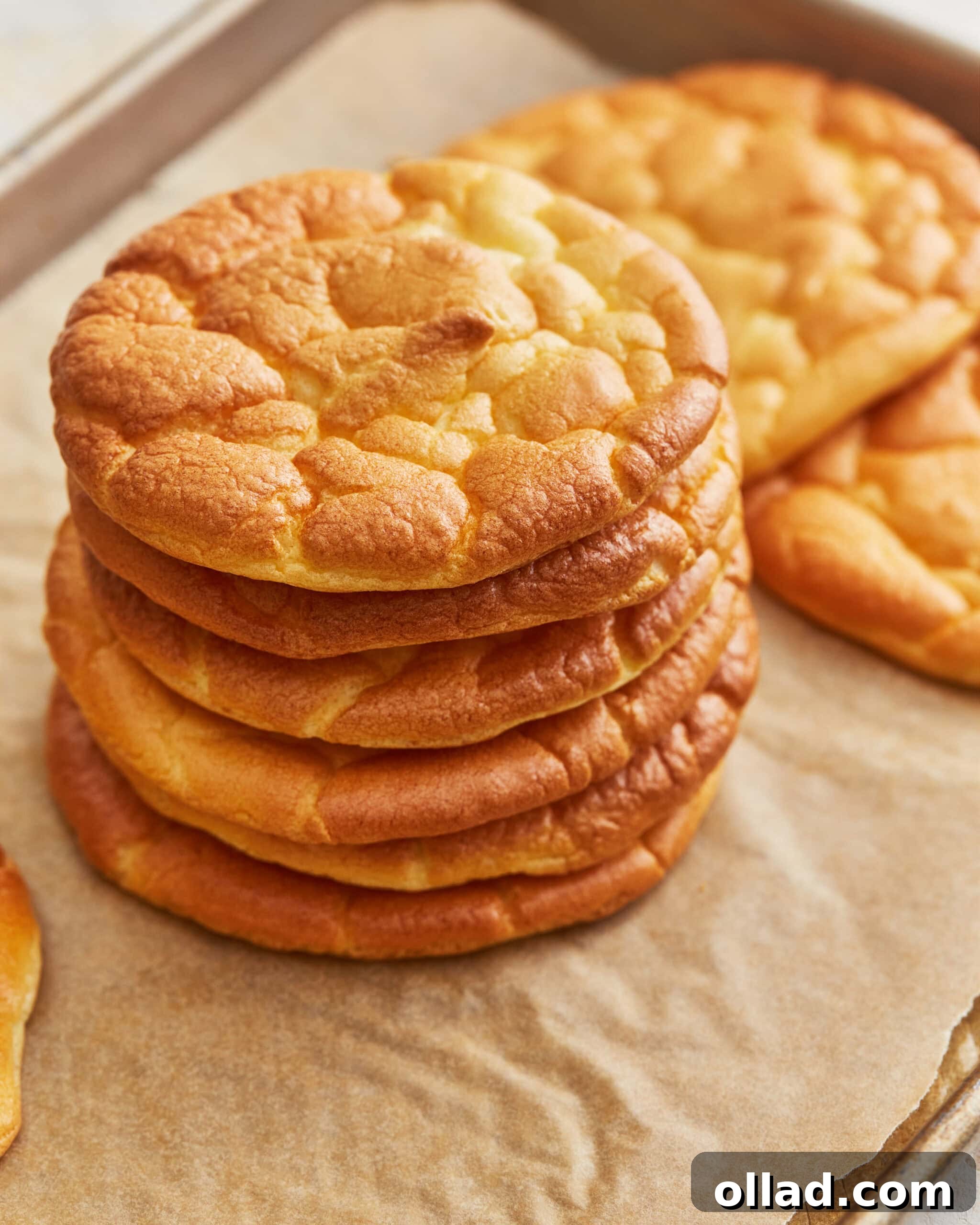 A stack of freshly baked cloud bread rounds on a parchment lined baking sheet, ready for storage or serving.