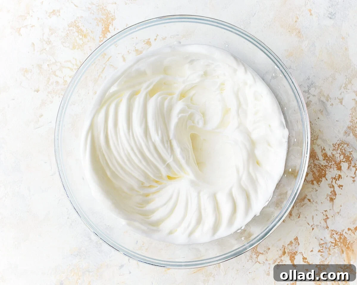 Whipped egg whites with cream of tartar in a large glass mixing bowl, showing stiff, glossy peaks.
