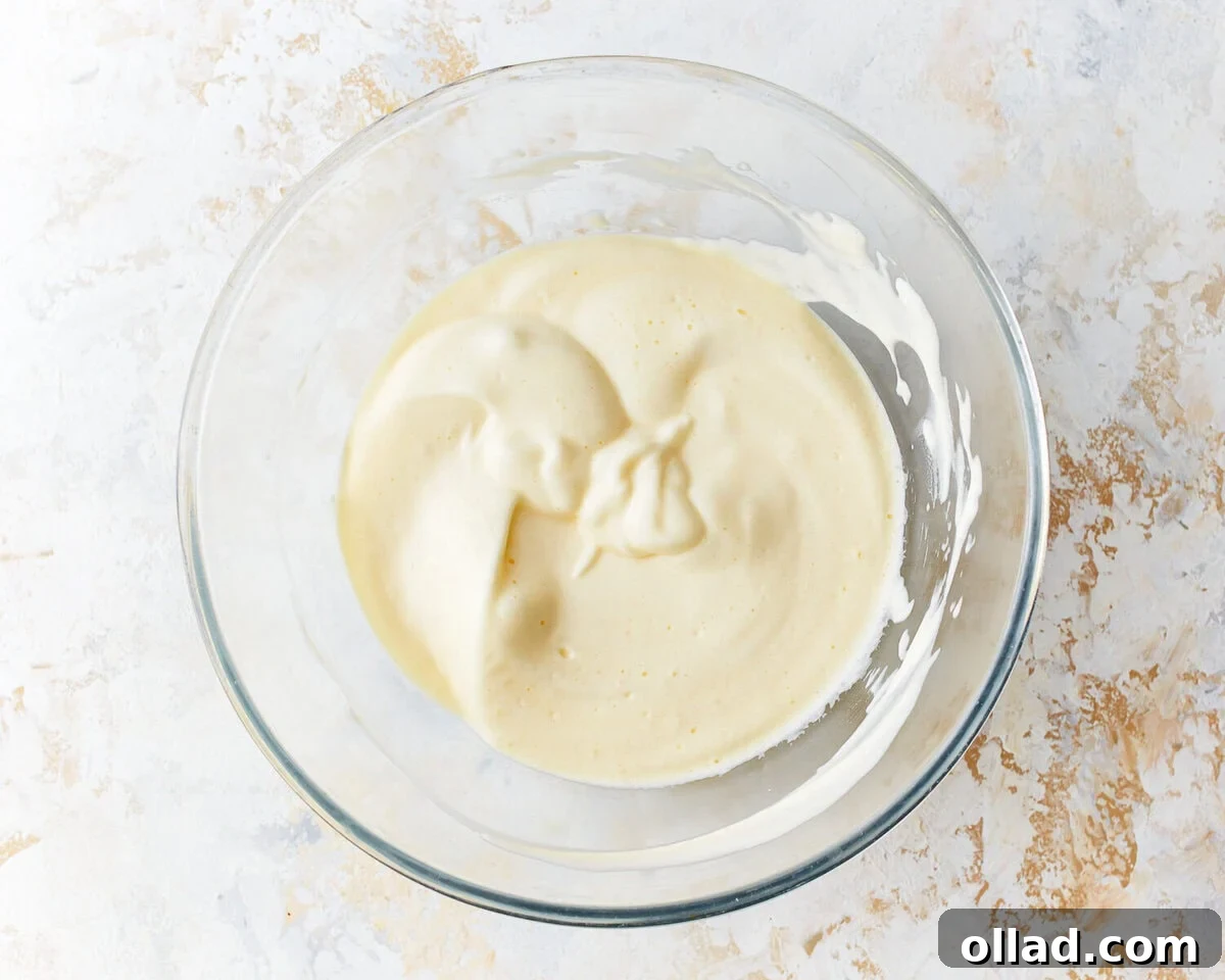 Egg white and cream cheese mixture gently folded together in a glass mixing bowl, maintaining airiness.