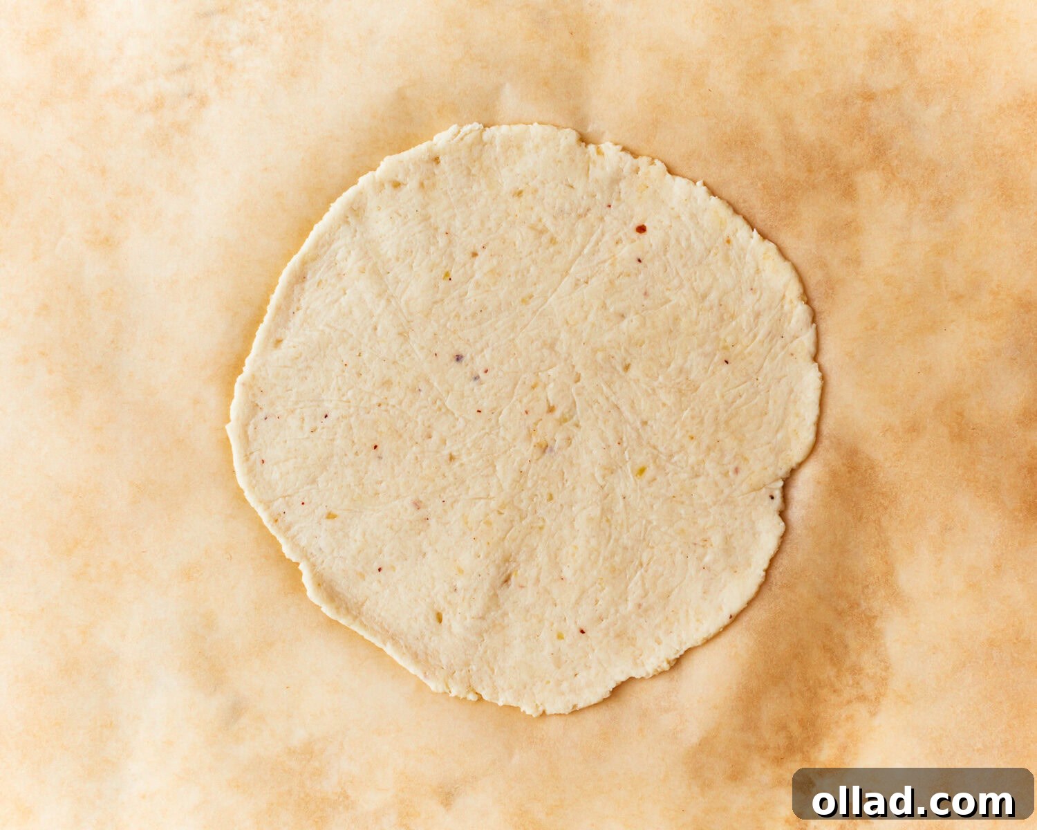 A perfectly rolled almond flour tortilla dough disc, thin and round, ready for cooking, resting on parchment paper.