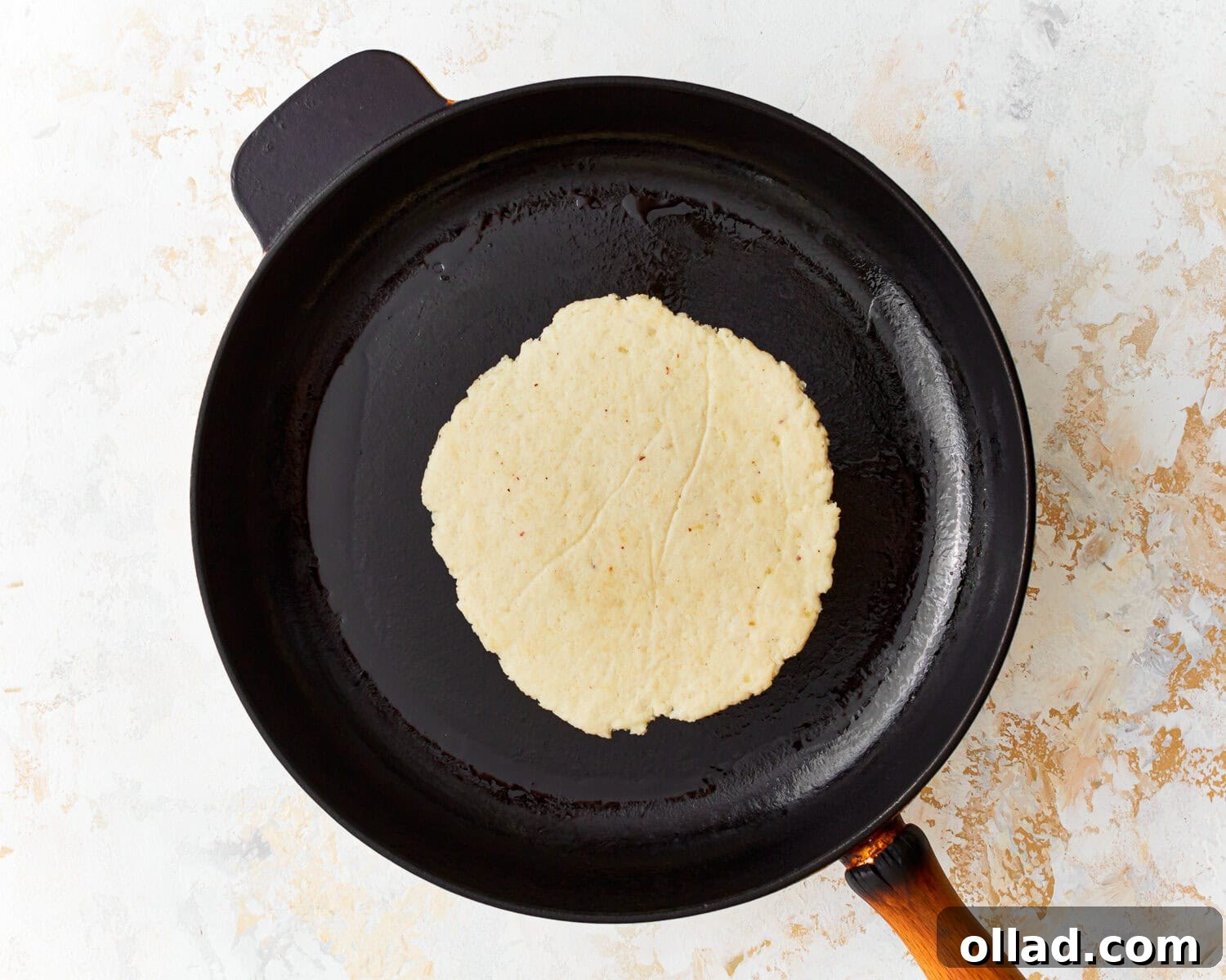 Overhead view of an almond flour tortilla sizzling gently in a preheated non-stick skillet, starting to develop appealing golden-brown spots.