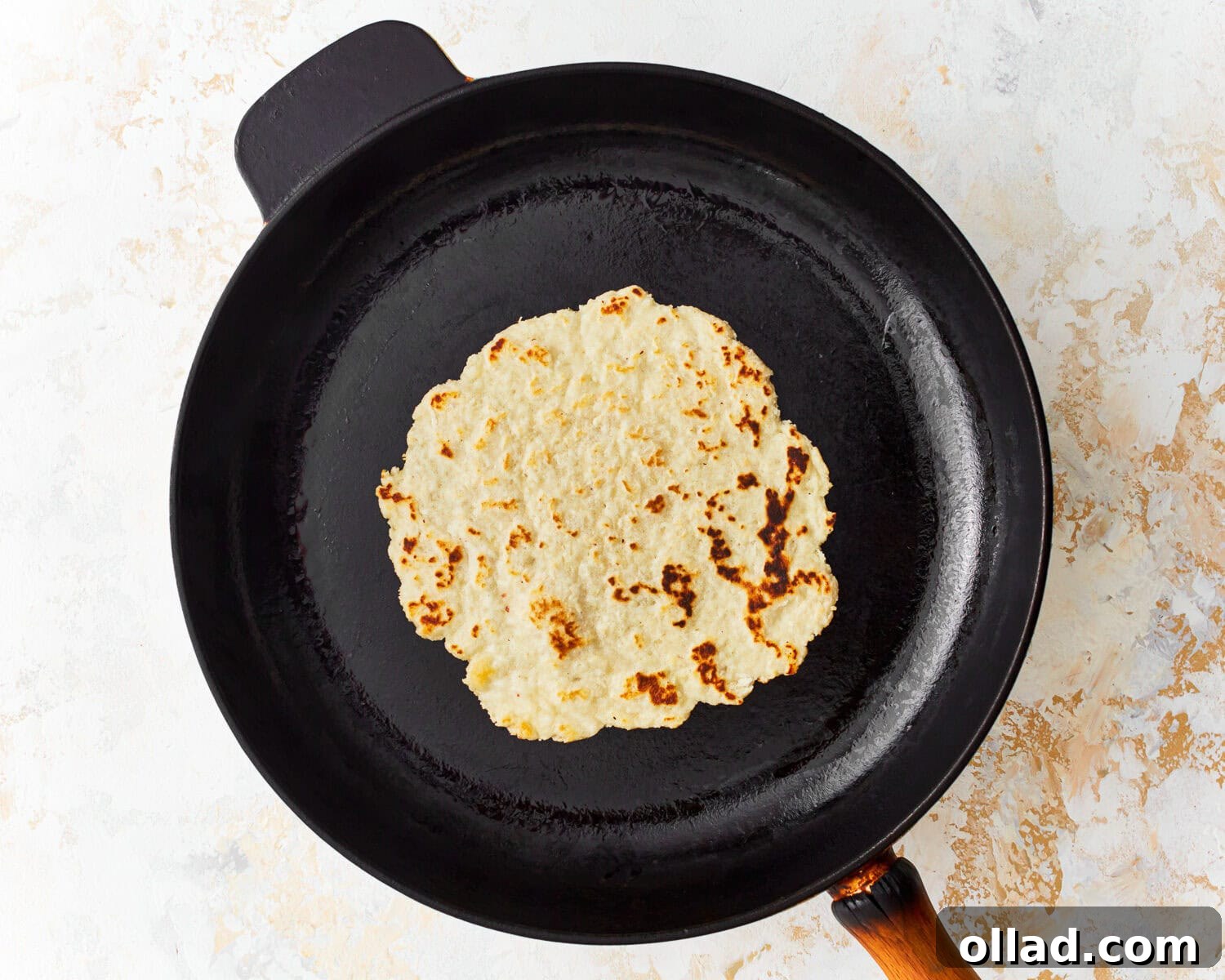 Overhead view of an almond flour tortilla freshly flipped over in a skillet, showcasing its perfectly golden-brown cooked side and ready for the final stage.