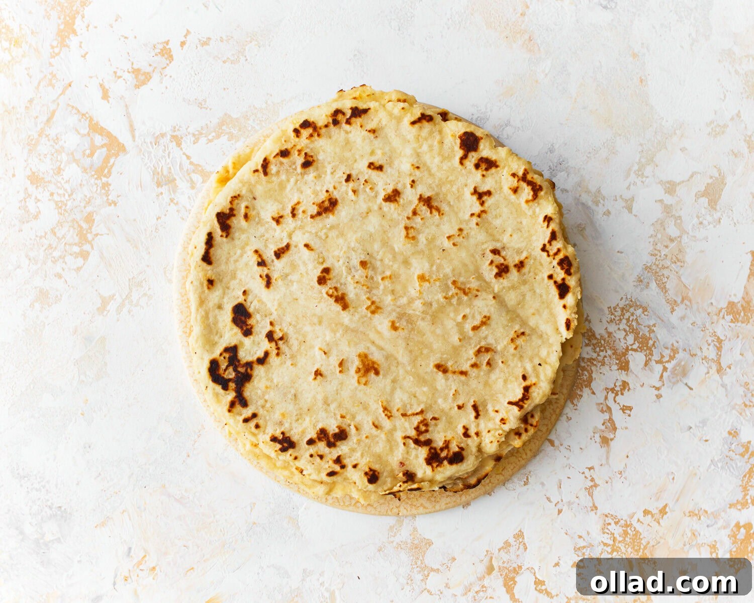 A inviting stack of freshly cooked almond flour tortillas, covered partially with a kitchen towel to retain warmth and softness, on a textured surface.