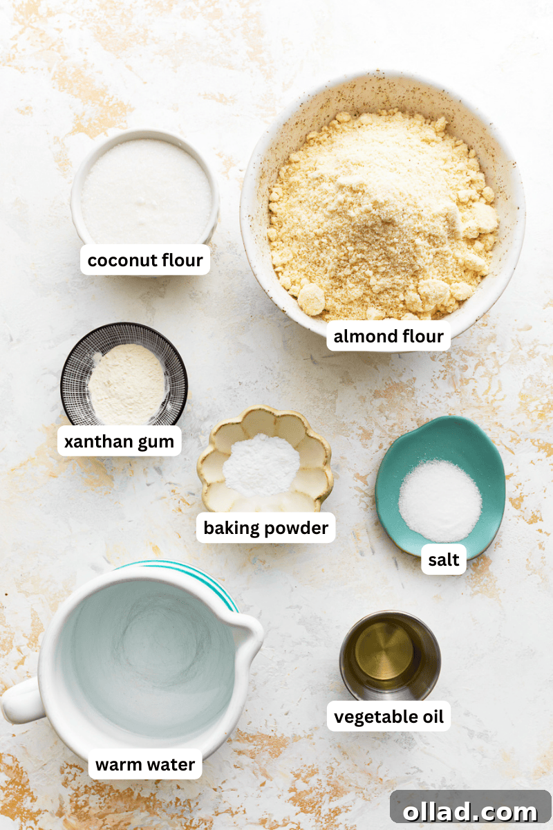 A collection of ingredients for almond flour tortillas, including blanched almond flour, coconut flour, xanthan gum, baking powder, salt, vegetable oil, and warm water, neatly arranged on a wooden surface.