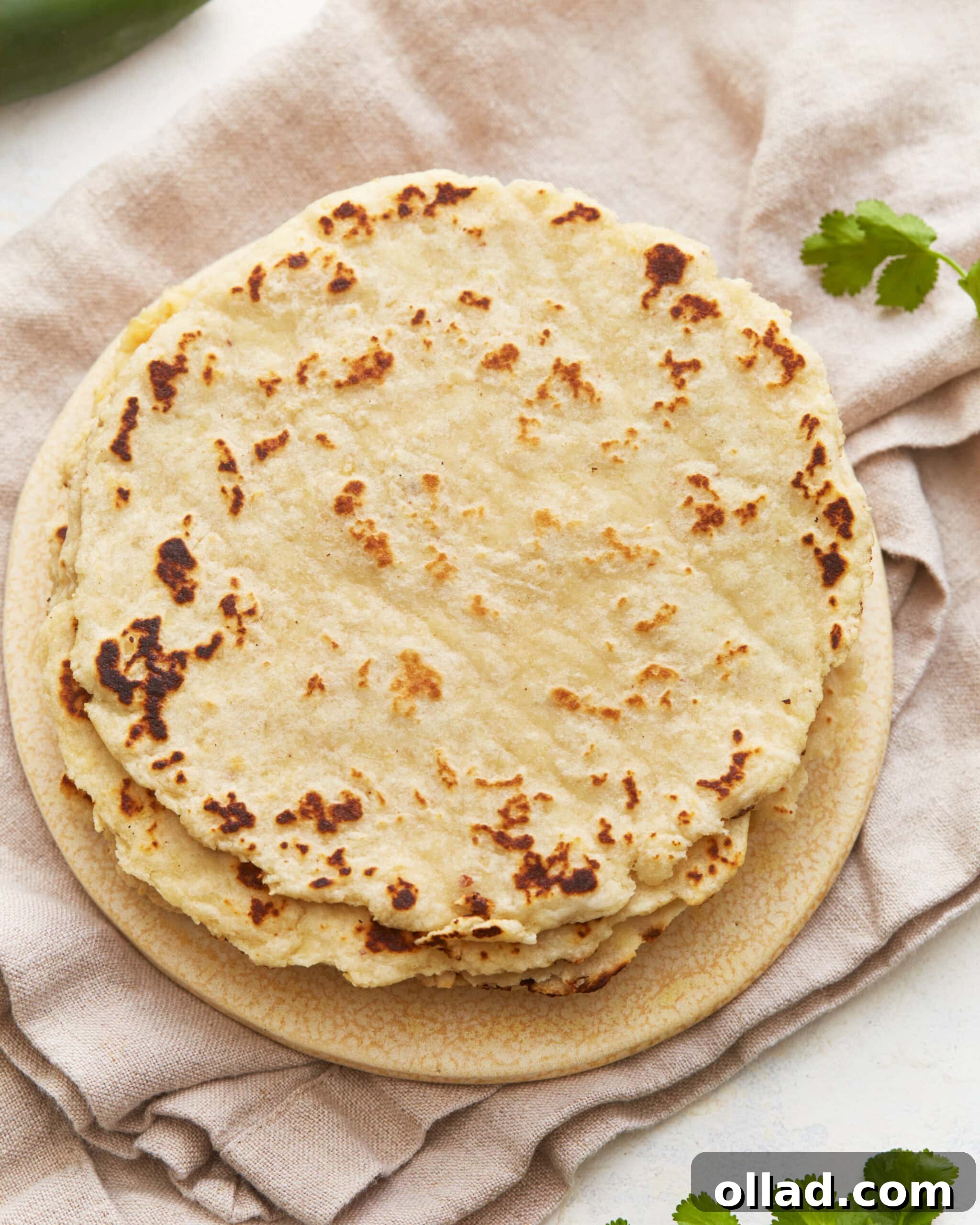 Overhead close-up view of a perfectly stacked pile of fresh almond flour tortillas, showcasing their soft, pliable texture and warm golden hue.