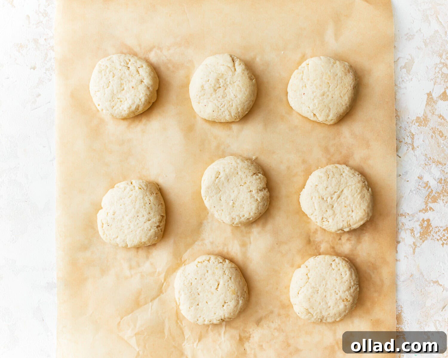 Eight portions of almond flour tortilla dough, neatly rolled into balls and resting on parchment paper on a baking sheet, covered with a kitchen towel.