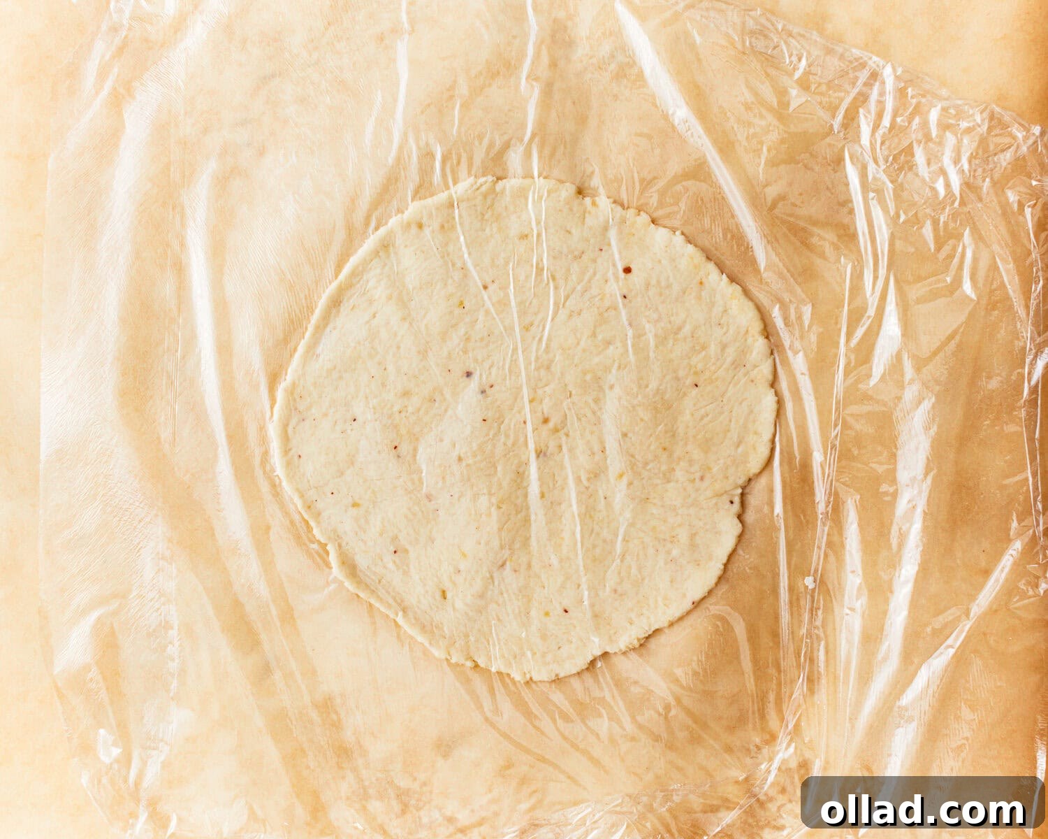 One portion of almond flour tortilla dough being rolled out thin between two sheets of parchment paper with a rolling pin on a cutting board.