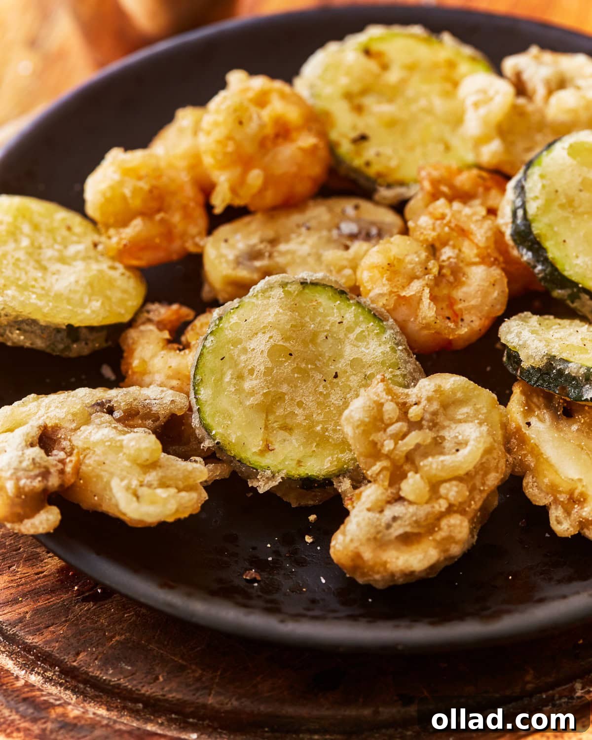 A plate of vegetables and shrimp cooked in a gluten free tempura batter, showing its golden and crispy texture.