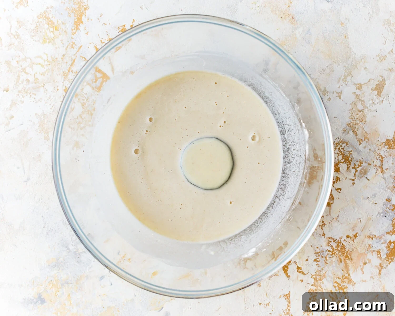 A slice of zucchini being dipped into the prepared gluten-free tempura batter in a clear mixing bowl.