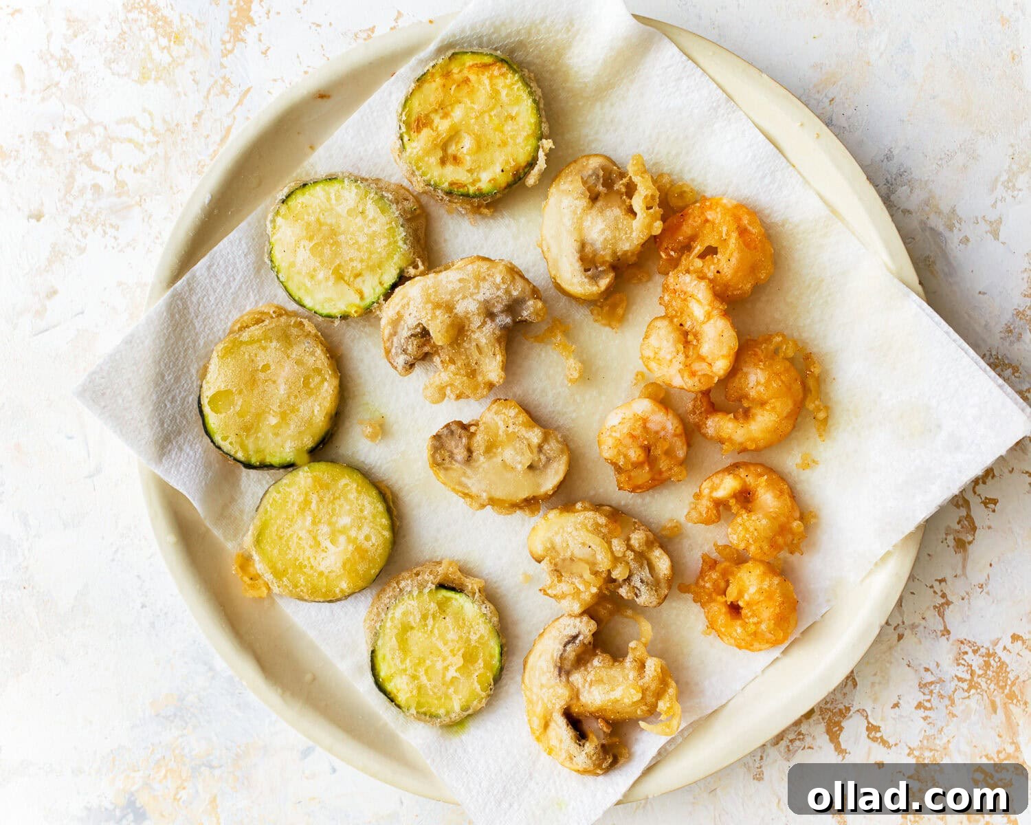 Freshly fried gluten-free tempura vegetables and shrimp draining on a paper towel-lined plate.