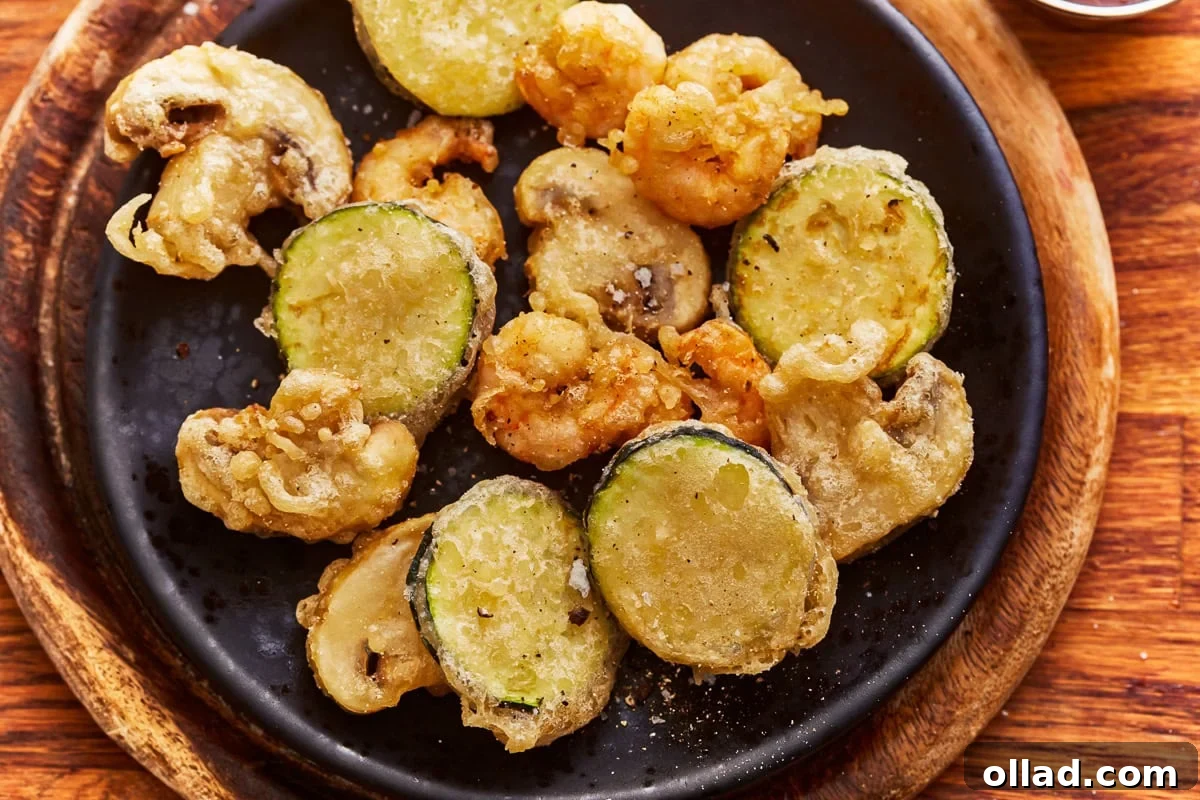 Overhead view of a plate of mixed vegetables and shrimp cooked in a gluten-free tempura batter, garnished with fresh herbs.