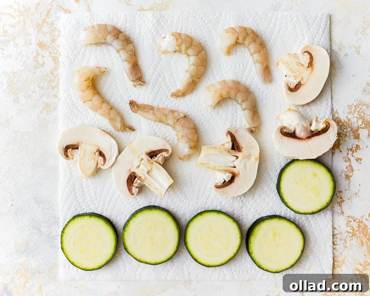 Prepared sliced zucchini, mushrooms, and shrimp resting on paper towels, ready for battering and frying.